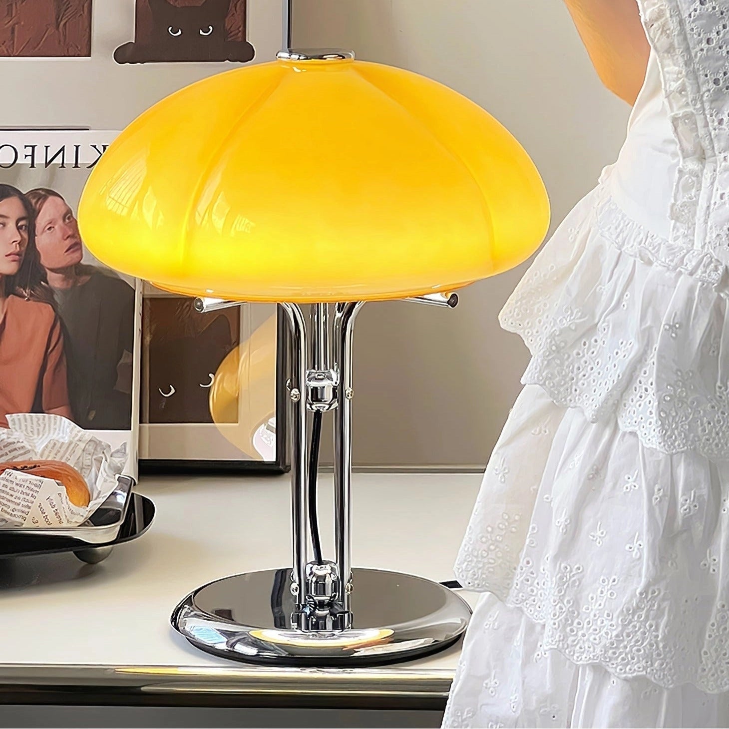 Modern orange globe table lamp with chrome base emitting warm light, placed on a table, ideal for interior design and decorative purposes.