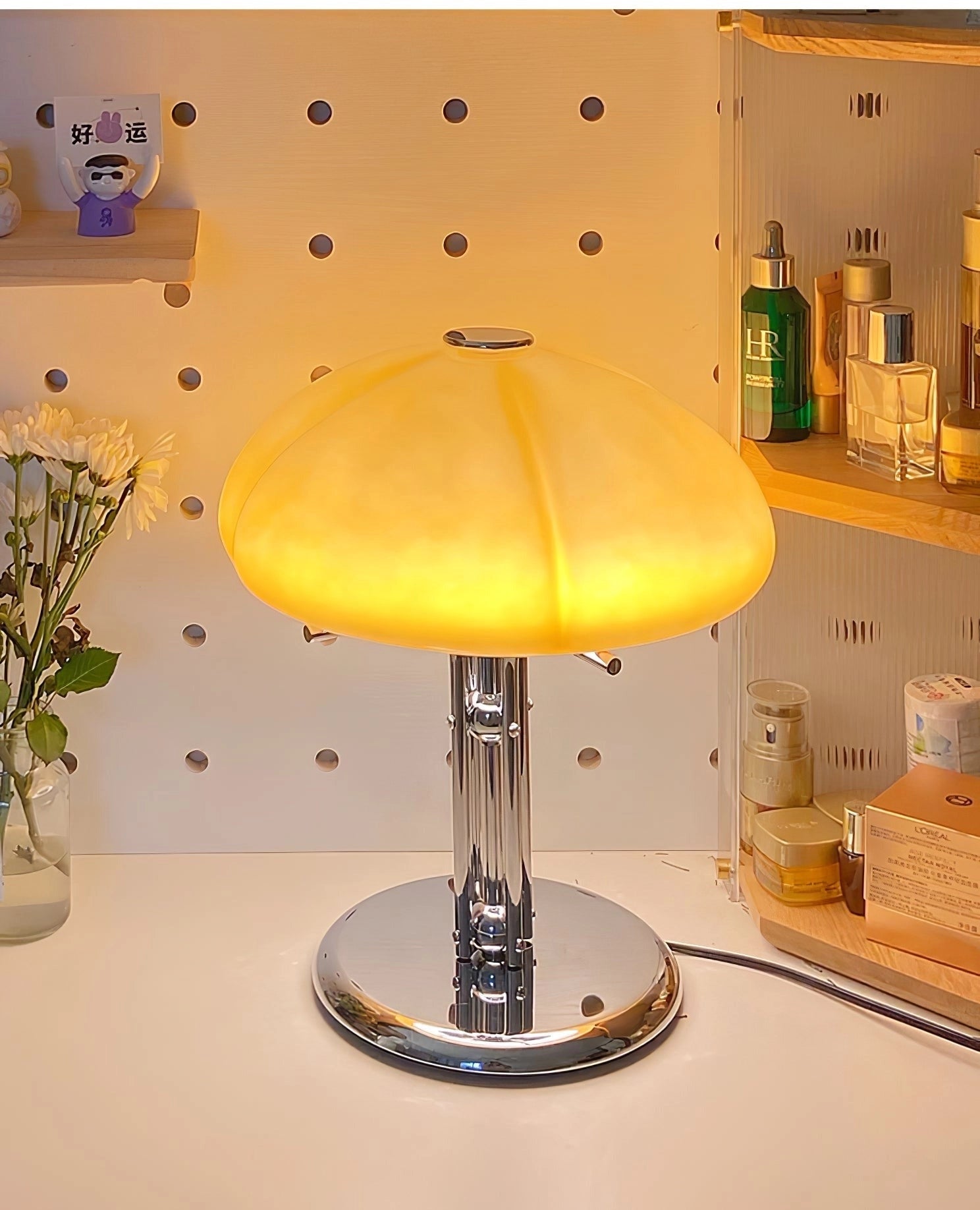 Modern orange globe table lamp with chrome base emitting warm light, placed on a wooden table next to a potted houseplant in a stylish interior setting.