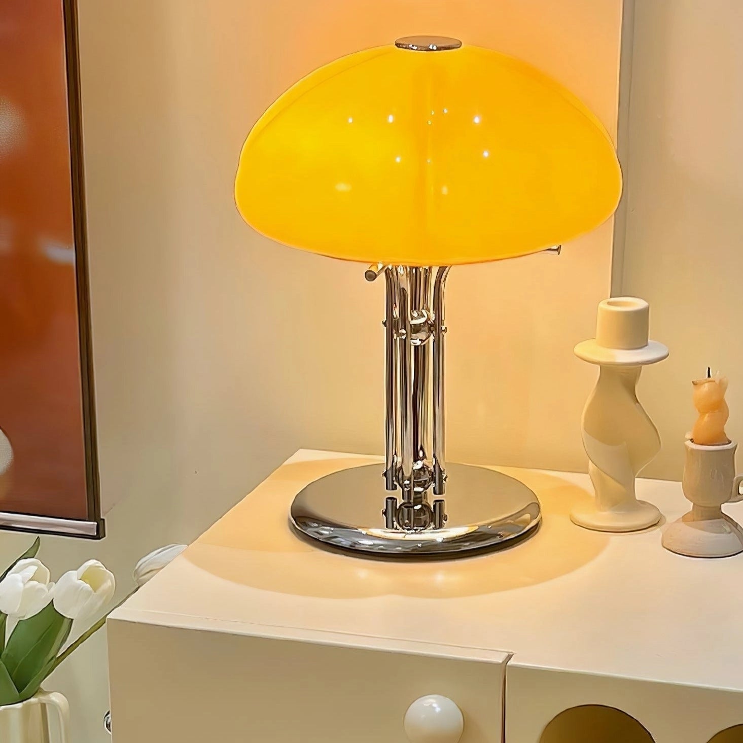 Modern orange globe table lamp with chrome base emitting warm light, placed on a wooden table in a stylish interior setting.