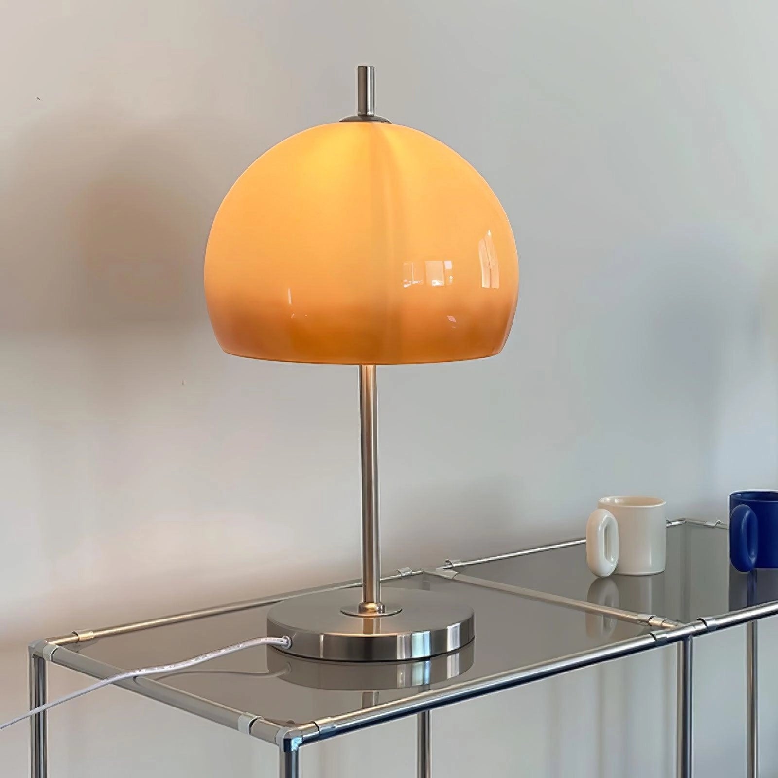 Modern orange globe table lamp with chrome base, emitting warm light, placed on a wooden table.
