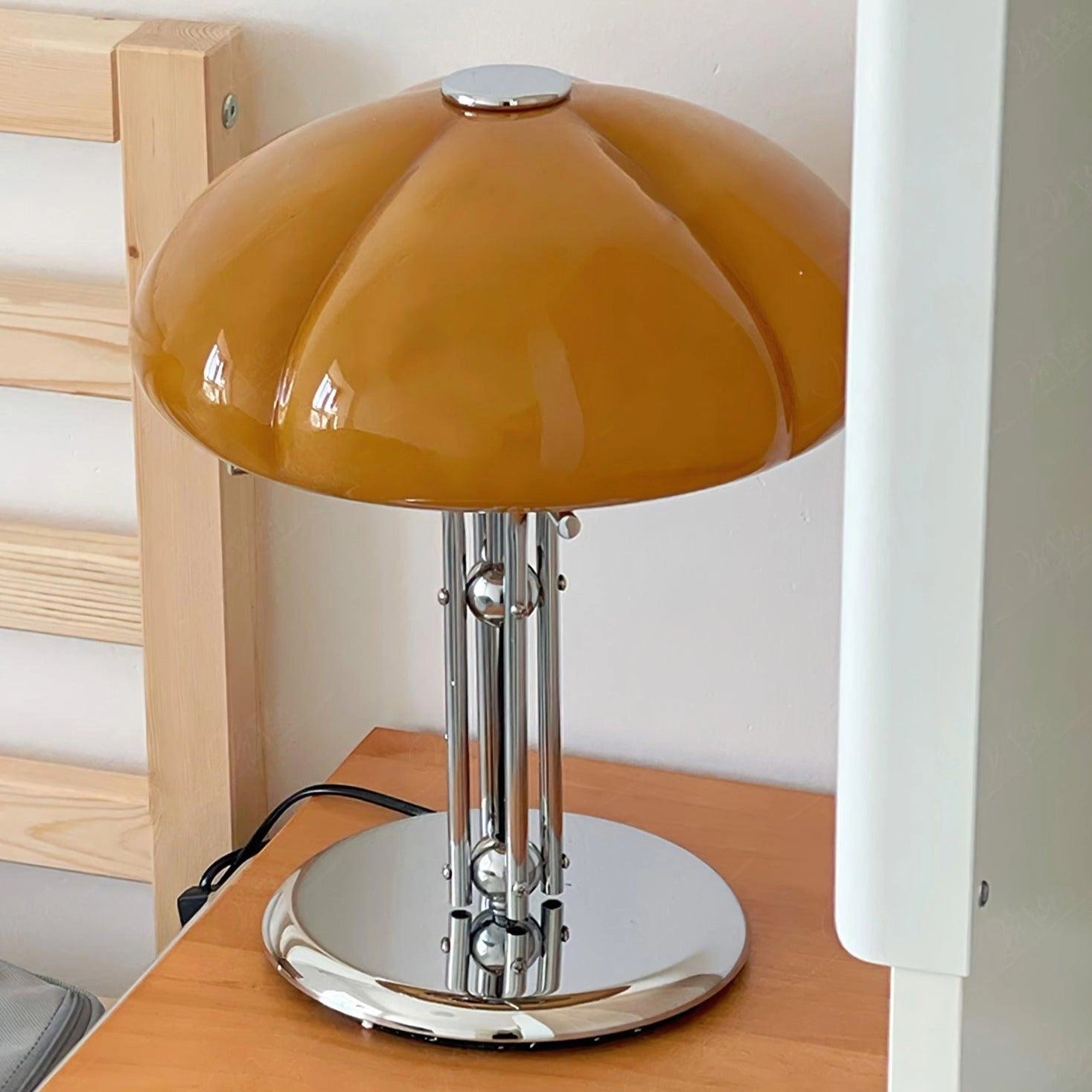 Modern orange globe table lamp with a chrome base and warm light, placed on a table.