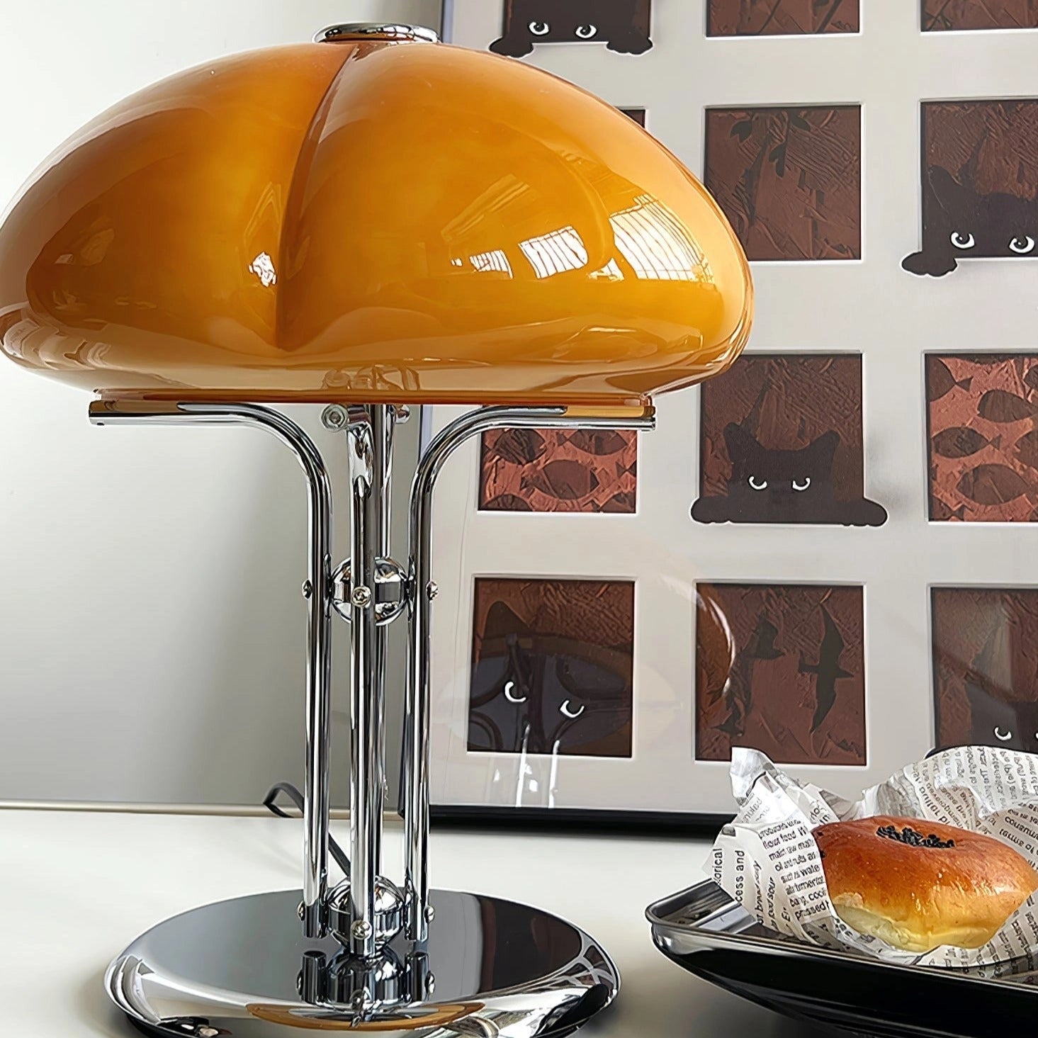 Modern orange globe table lamp with chrome base and warm light, positioned on a table.