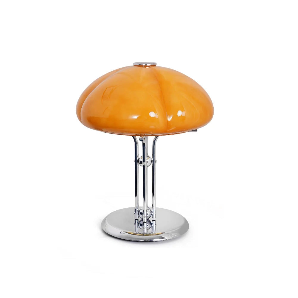 Modern orange globe table lamp with chrome base, emitting warm light, placed on a wooden surface with a small plant nearby.