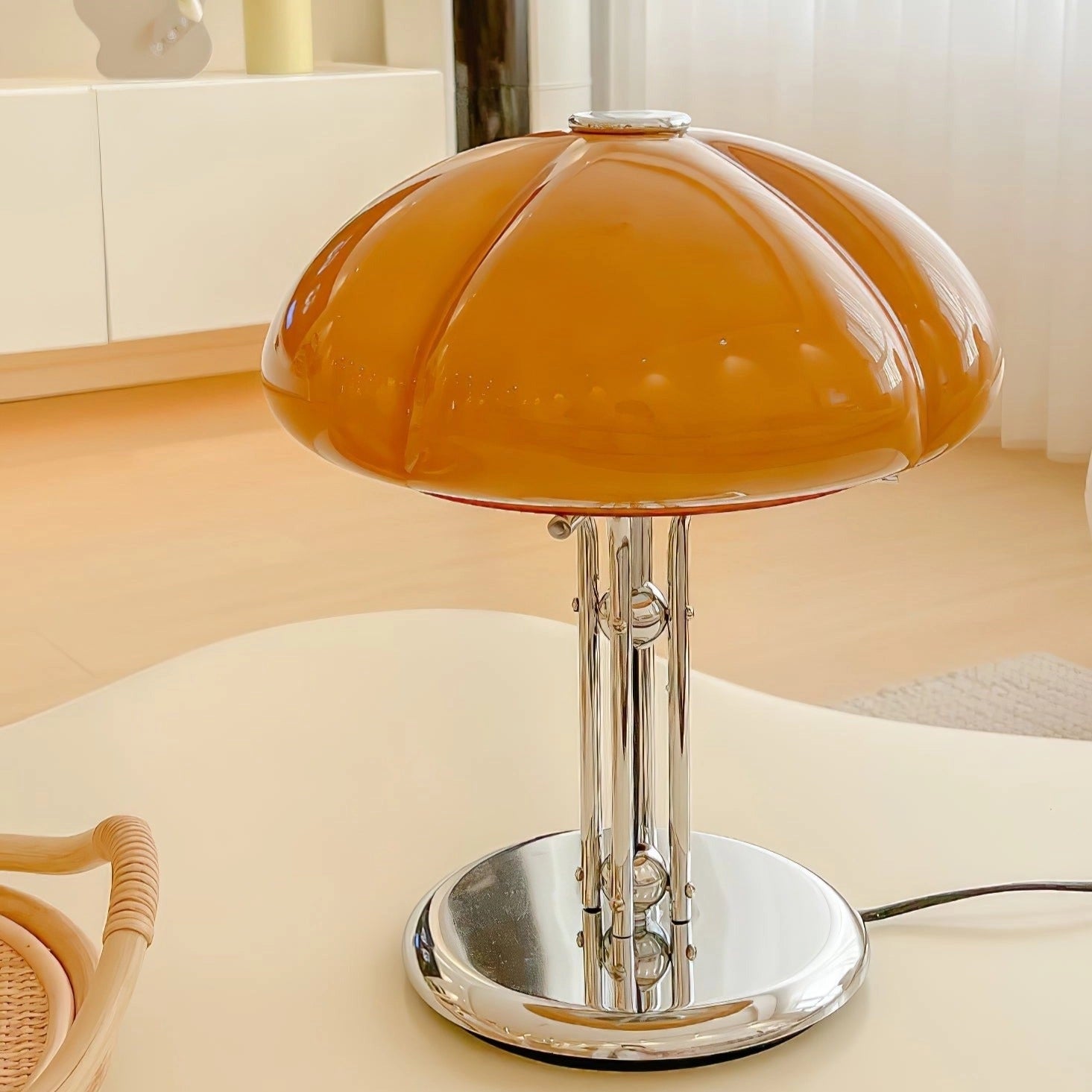 Modern orange globe table lamp with chrome base emitting warm light, placed on a wooden table.