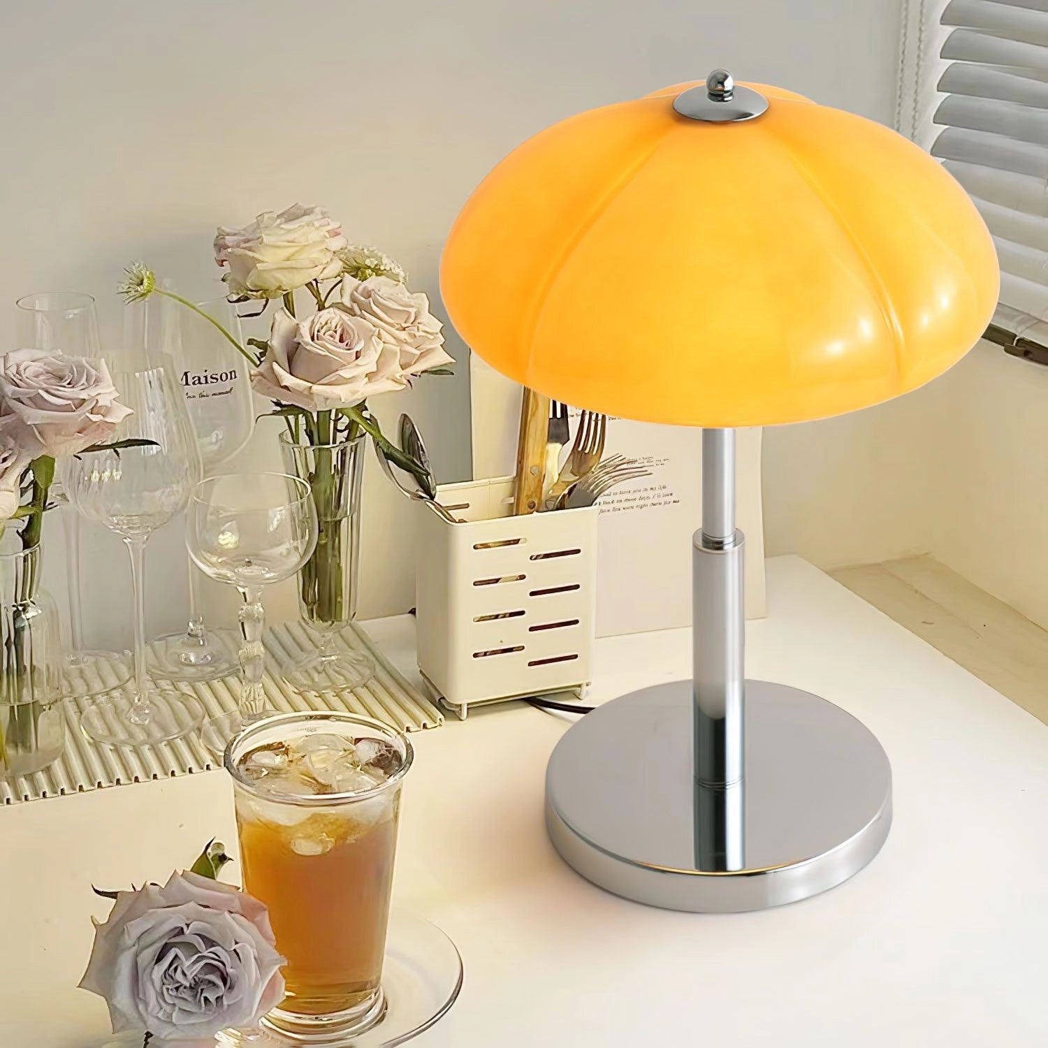 Modern orange globe table lamp with chrome base emitting warm light, model B, dimensions Ø 11.8″ x H 14.2″, placed on a table with decorative elements.