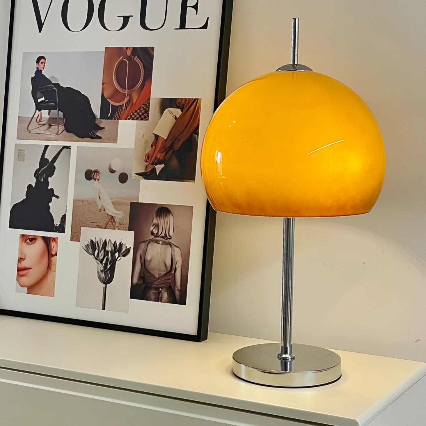 Modern orange globe table lamp with chrome base and warm light, placed on a table next to a picture frame.
