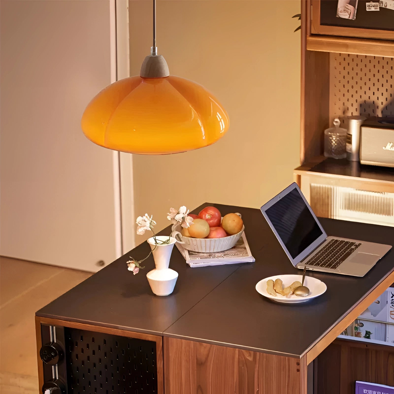 Modern orange pendant lamp hanging above a wooden table with a laptop, highlighting contemporary home office and kitchen lighting.