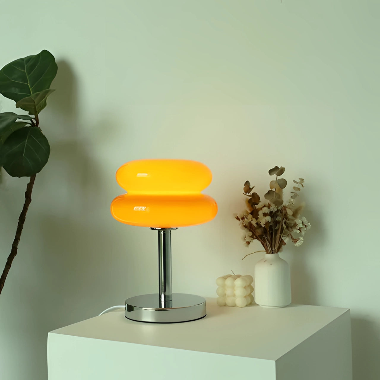 Modern orange spiral table lamp with a stylish base, featuring an LED light. The lamp is positioned on a table in a contemporary interior setting, accompanied by a plant and decorative vase, with shelving and a wall in the background. The variant shown is bright orange with USB compatibility.
