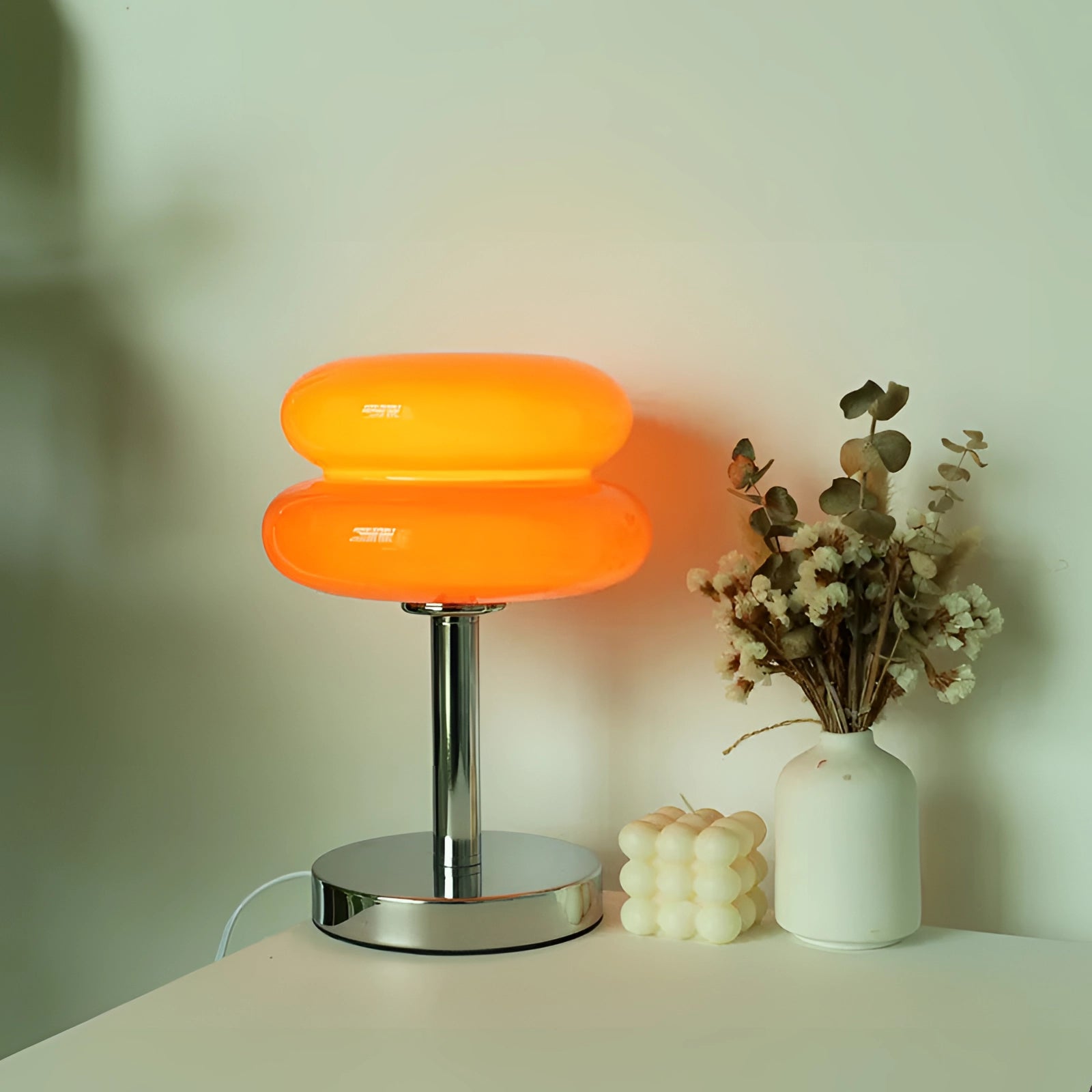 Modern orange spiral table lamp with a sleek designer LED feature and a stylish base, placed on a wooden table next to a small flowerpot with green plants, against a neutral background.