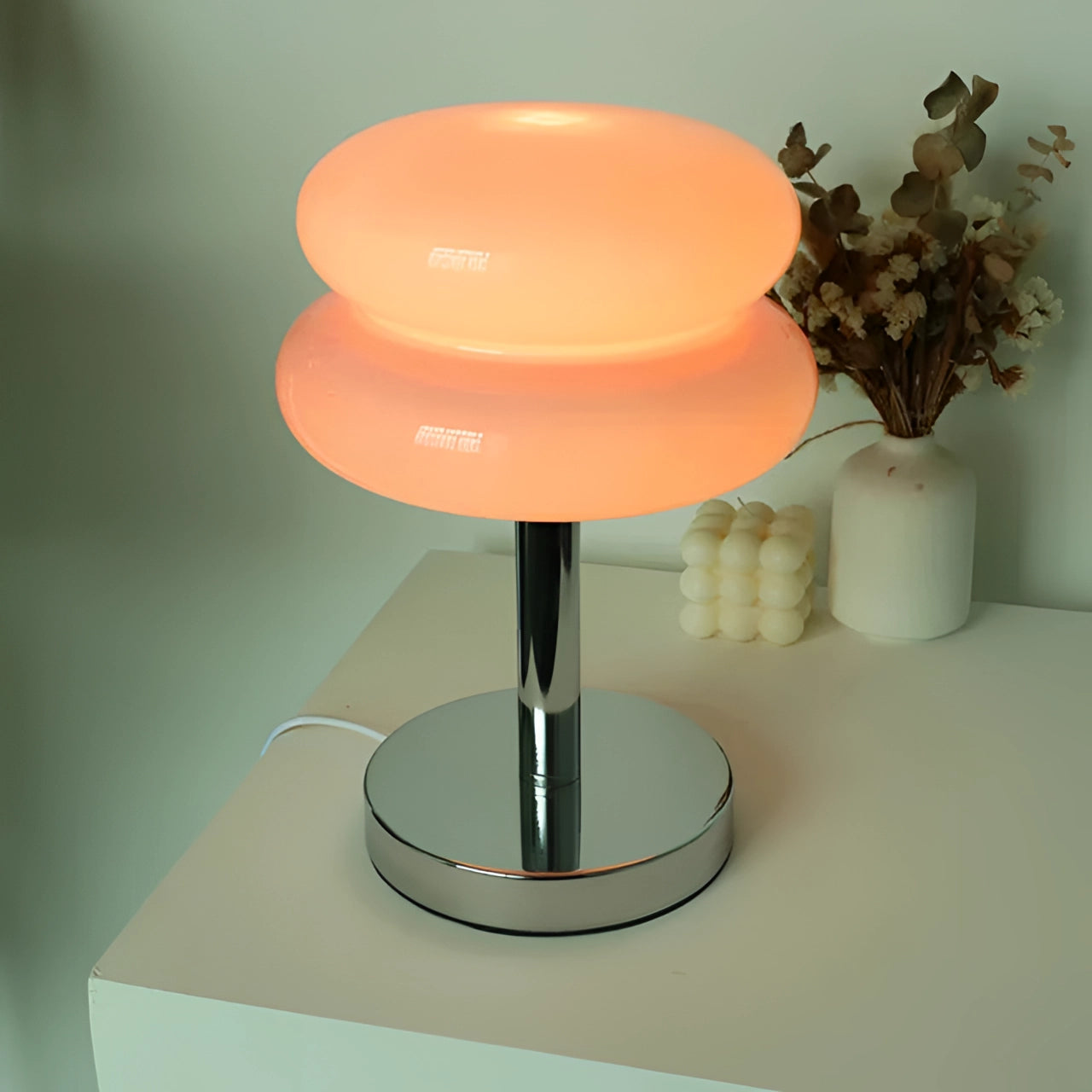 Modern orange spiral table lamp with a stylish base, featuring pink accents and a USB port, placed on a table surface with artistic decor elements. The lamp stands out against a neutral background with hints of peach and magenta tones.