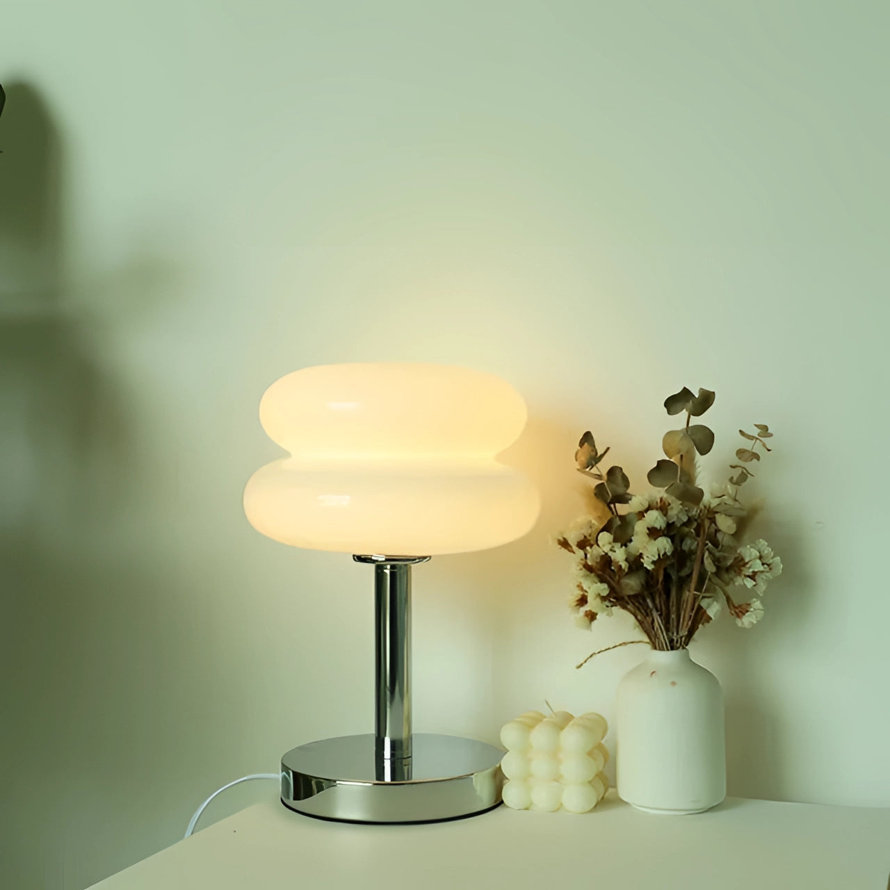 Modern orange spiral table lamp with a stylish base and designer LED lighting, featuring a white variant with USB compatibility. The lamp is placed on a table alongside a small plant and a decorative vase, with wood flooring and a ceiling visible in the background.