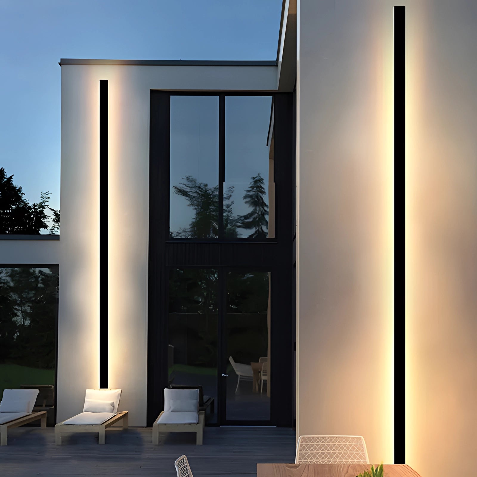 Modern outdoor LED wall light with a slim, minimalist design mounted on a building exterior, showcasing its energy-efficient illumination. The surrounding architecture includes wood elements and is complemented by a clear sky and lush greenery.