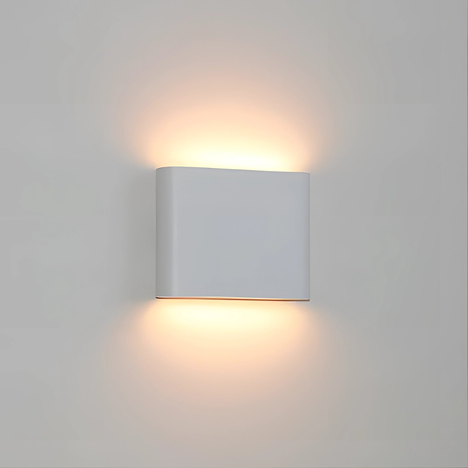 Modern outdoor LED wall sconce in white, featuring a rectangular design with a warm white light. Made from weather-resistant materials, it is mounted on a wall, showcasing a sleek and minimalist style suitable for contemporary exteriors.