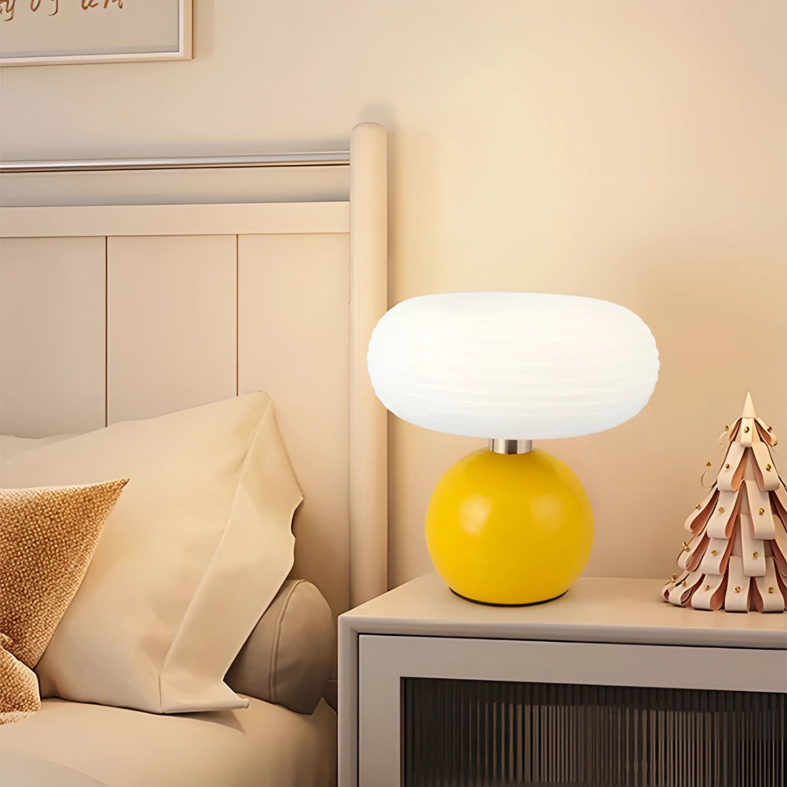 Modern oval glass bedside lamp with a minimalist frosted design, emitting a warm yellow light, placed on a wooden table against a white and orange interior setting.