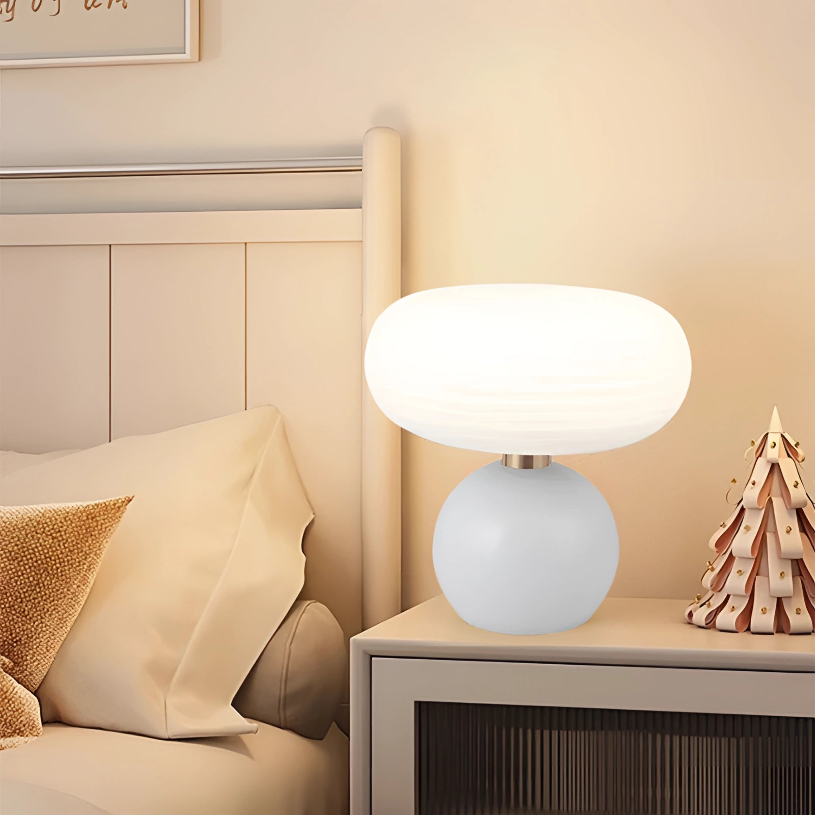 Modern oval glass bedside lamp with a minimalist frosted design in white, placed on a wooden table, complementing a beige and white interior setup.