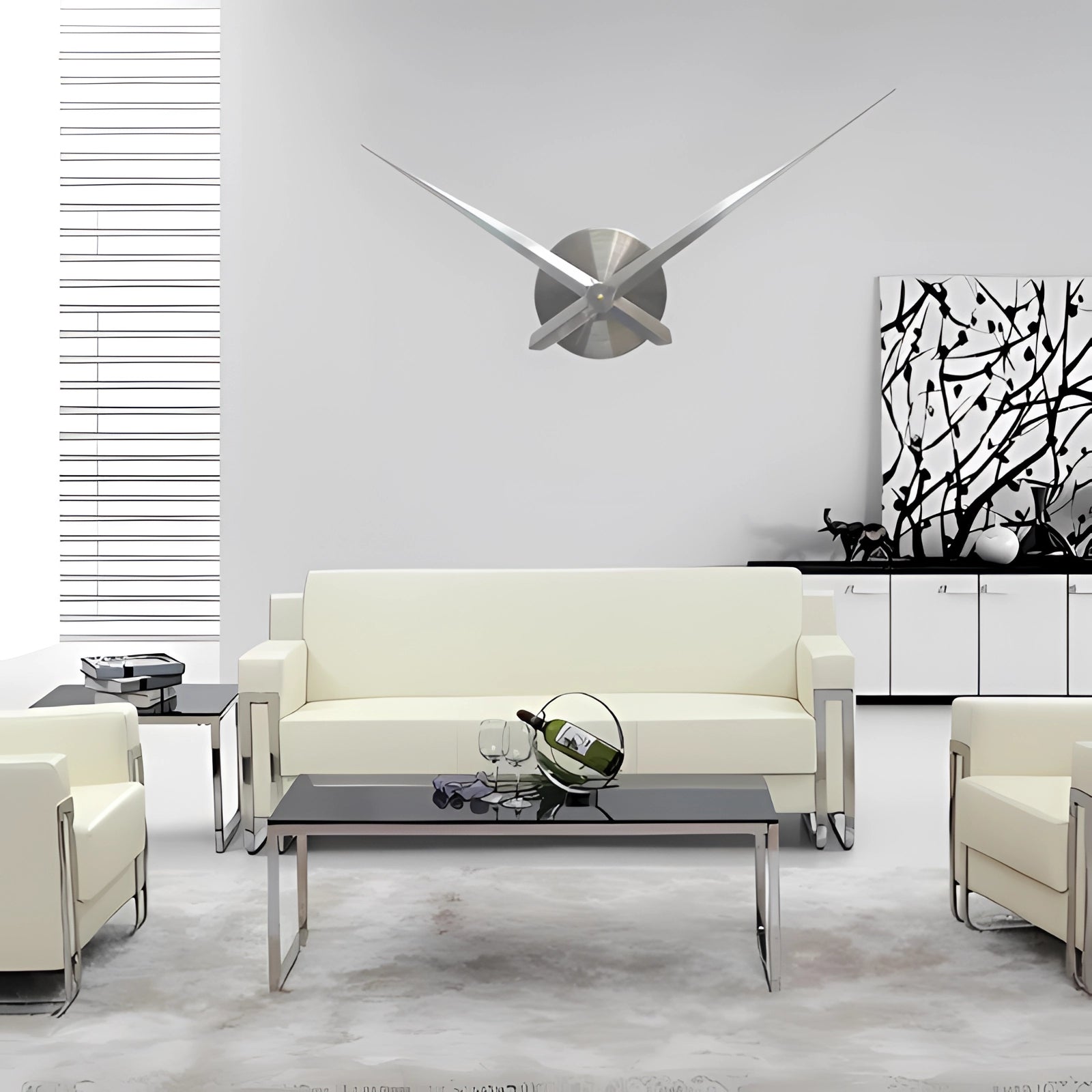 Modern oversized black wall clock with a minimalist design featuring silver accents, mounted on a white wall in a stylish interior setting with grey and black furniture.