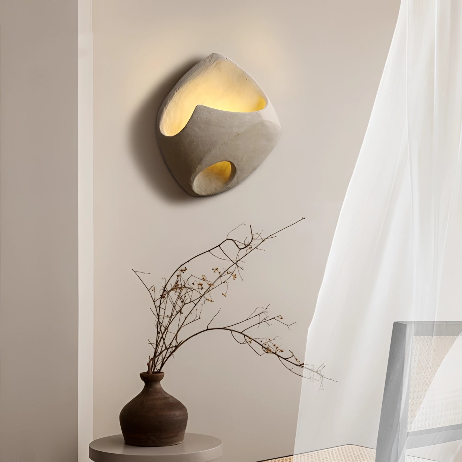 Modern pebble wall lamp illuminating a stylish interior setting with a stone look, featuring houseplants in vases and artful decor elements against a textured wall.