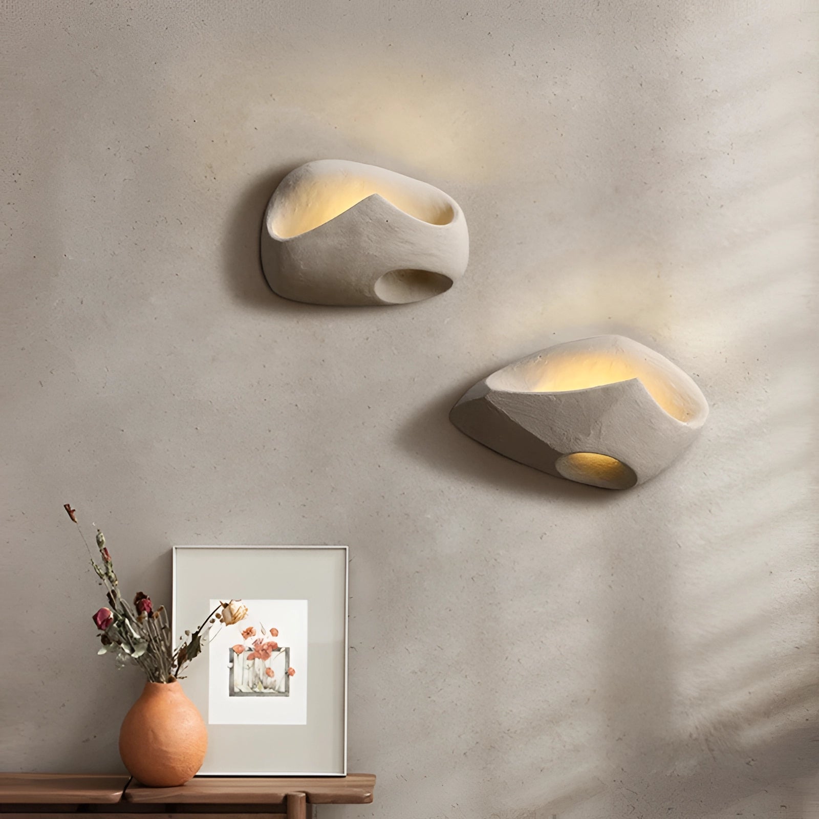 Modern pebble wall lamp with a stone look mounted on a wall, surrounded by houseplants and decorative flowerpots, adding a natural and artistic touch to the indoor space.