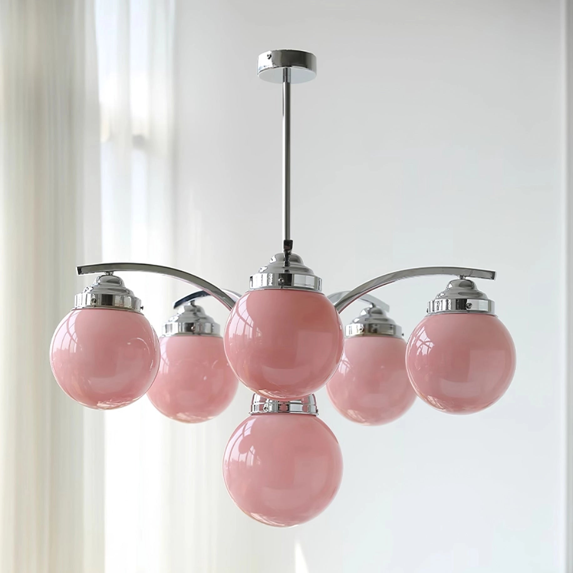 Modern pink glass chandelier with elegant minimalist design, featuring circular silver metal frame and delicate branching elements, hanging from ceiling.