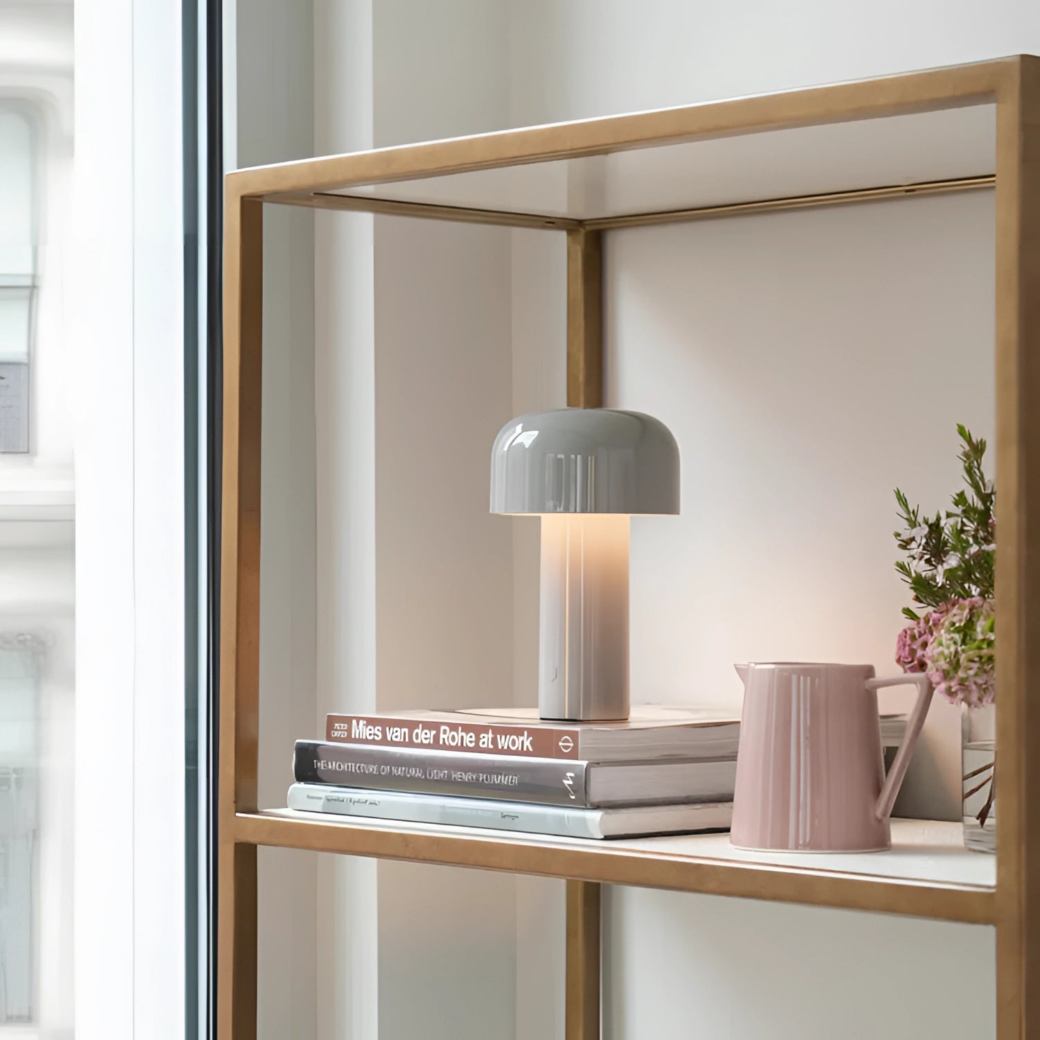 A modern portable wireless LED lamp with a sleek design and touch control, placed on a wooden shelf alongside a potted plant, a vase, and cabinetry, showcasing a stylish interior design setting.