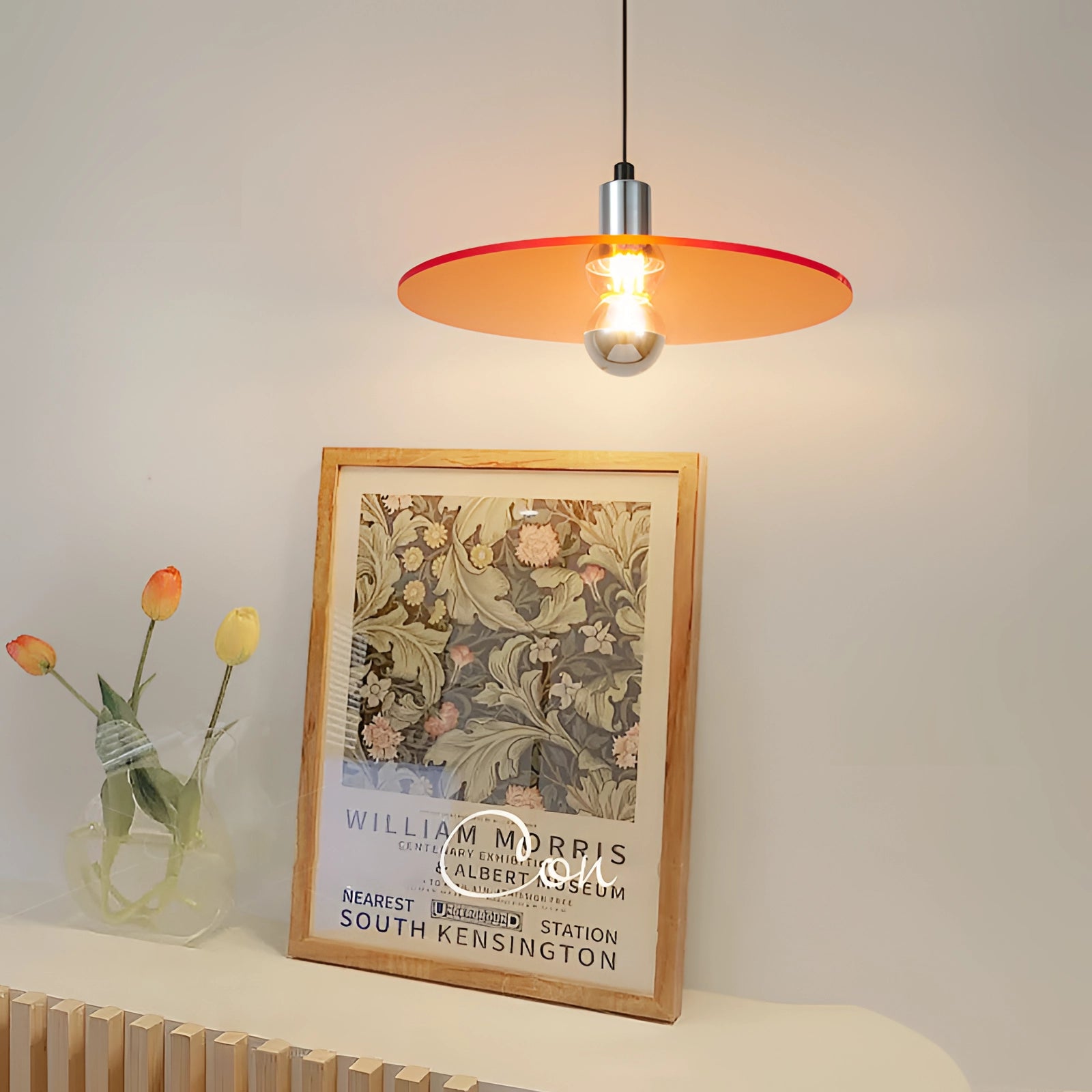 Modern orange metallic pendant light with an industrial design hanging from the ceiling, surrounded by wooden elements and plants.
