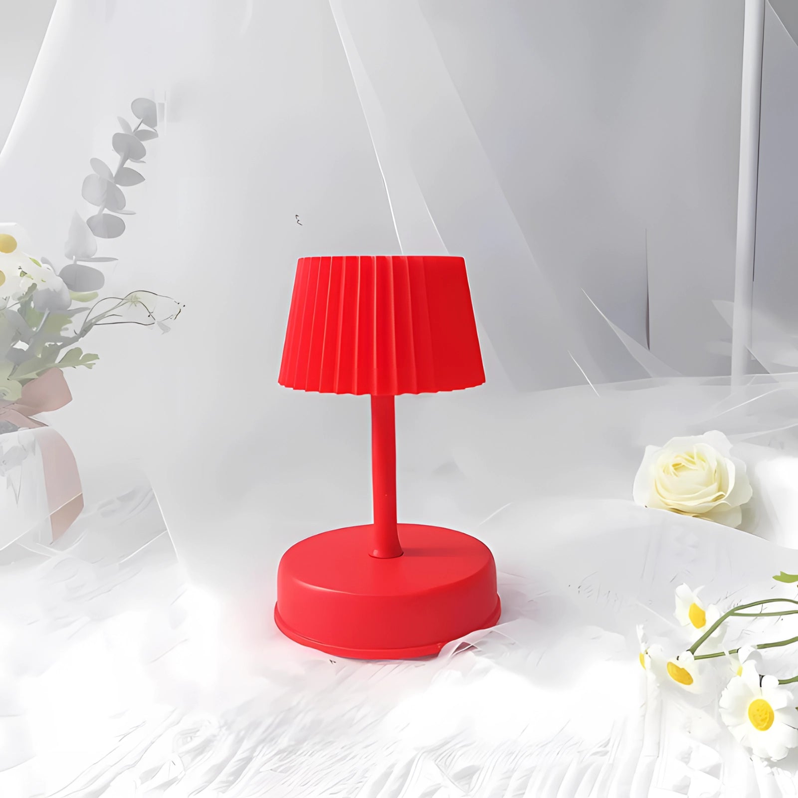 Modern red table lamp with a pleated lampshade placed on a wooden surface, surrounded by contemporary interior elements including a plant and decorative flooring.
