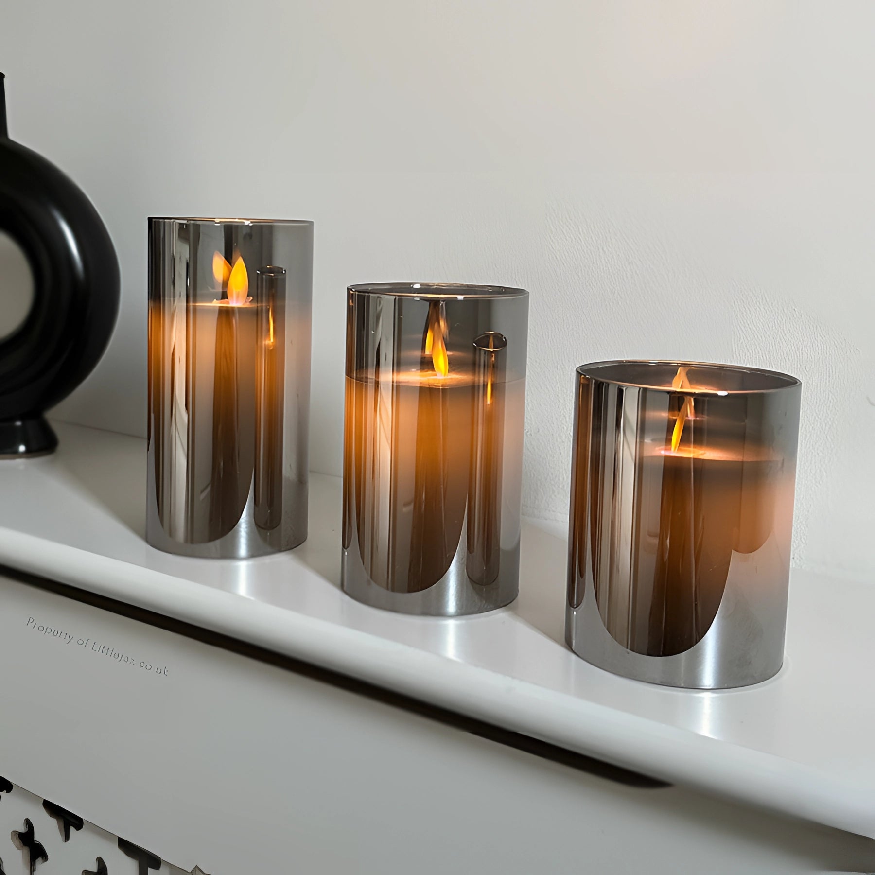 Modern reflective glass candle holders with a minimalist design, featuring cylindrical shapes that elegantly display candles. The holders are likely set on a wooden surface, creating a sophisticated and artful ambiance.