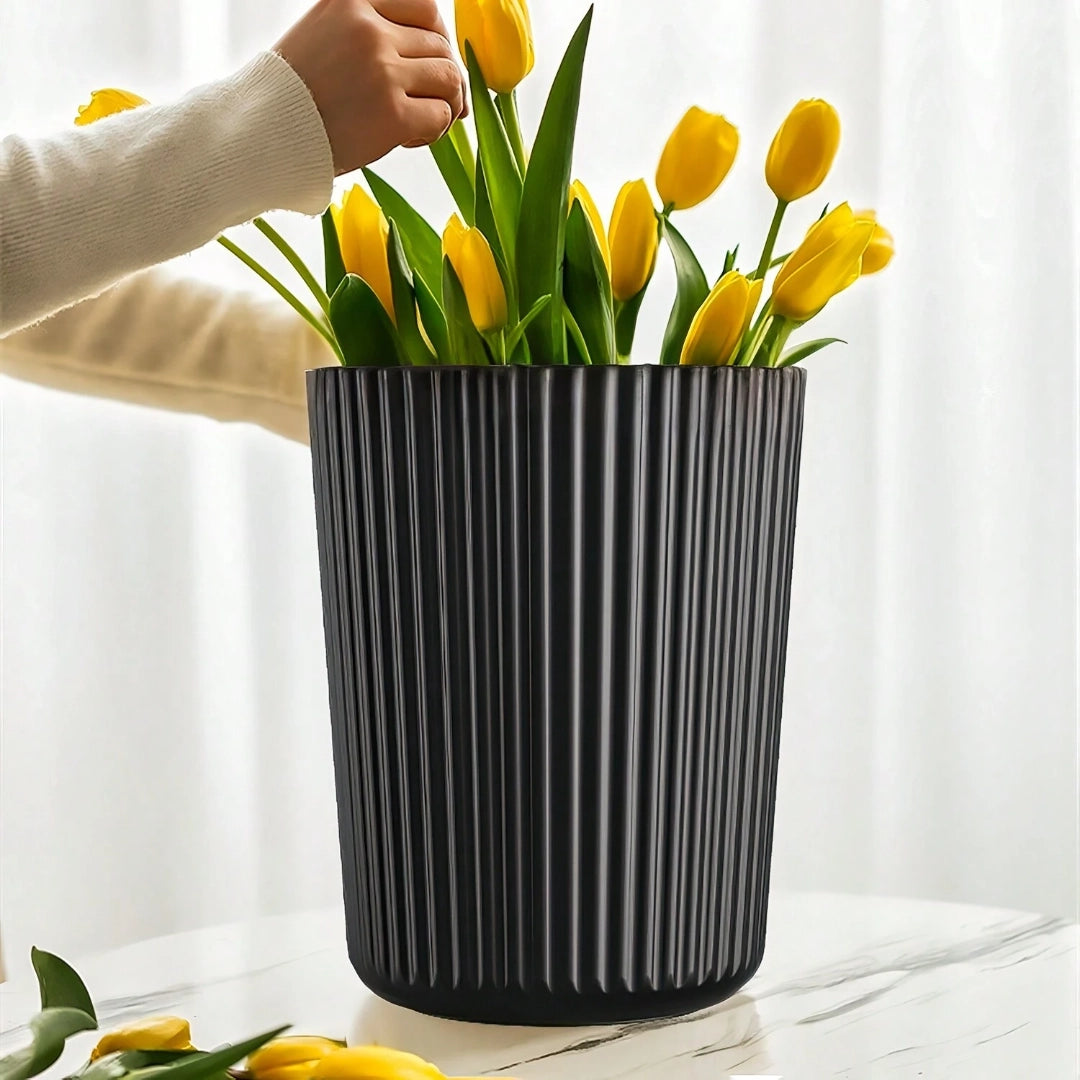 A modern ribbed ceramic planter in a Scandinavian design, featuring a vibrant yellow flower arrangement with green grass-like foliage, displayed on a tabletop.
