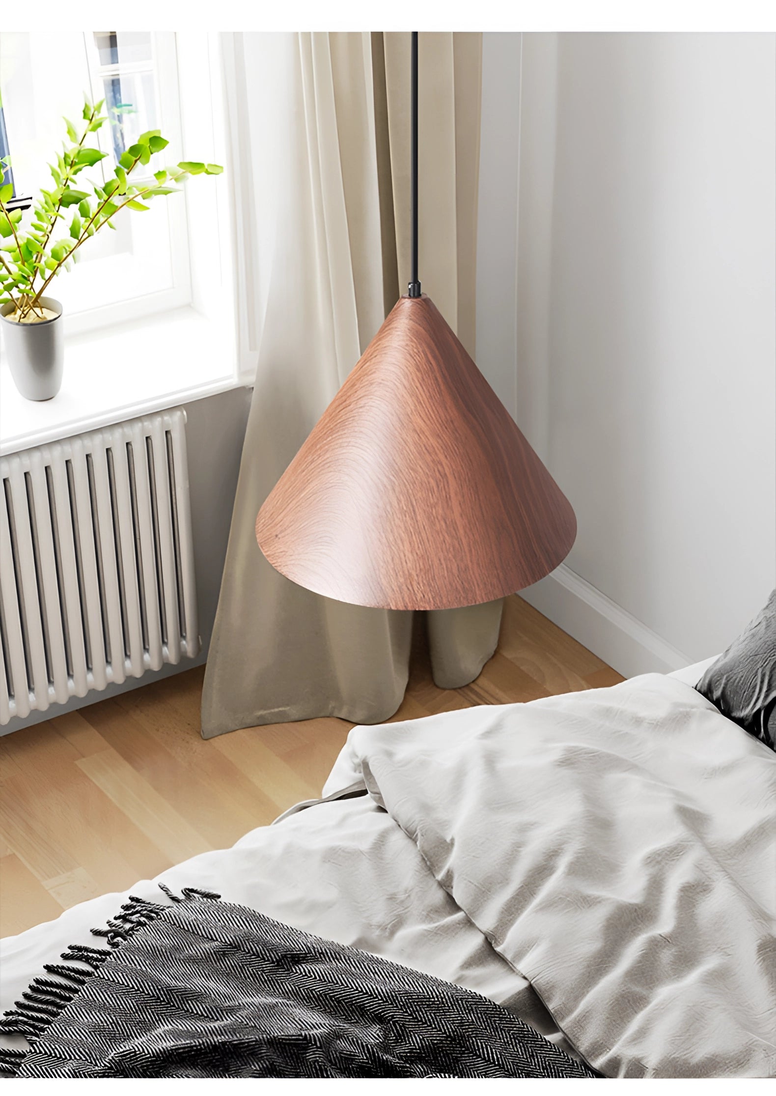 Modern Scandinavian eco-friendly triangle wooden pendant light with a wooden shade, hanging above a softly-lit room featuring houseplants and a textile-covered bed frame.