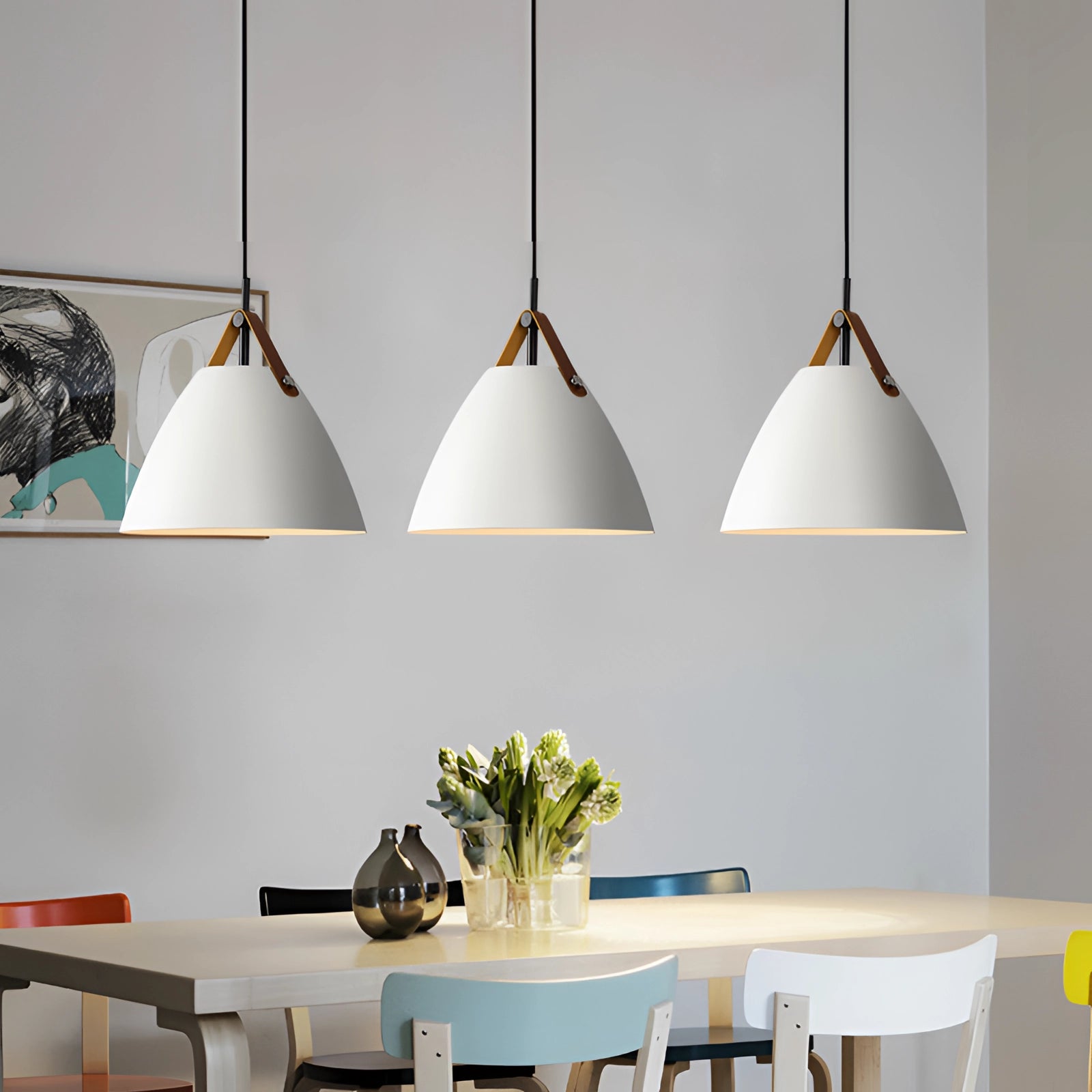 Modern Scandinavian pendant lights in black and white hanging above a wooden table with a potted plant, illuminating the interior space with bright, adjustable lighting.