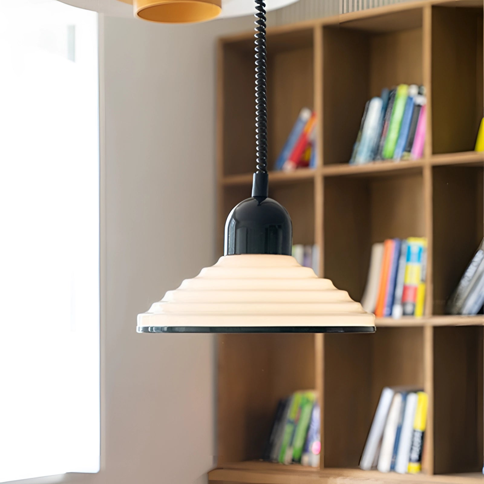 Modern Scandinavian white acrylic pendant light hanging from the ceiling, illuminating a minimalistic interior space with shelves and books in the background.