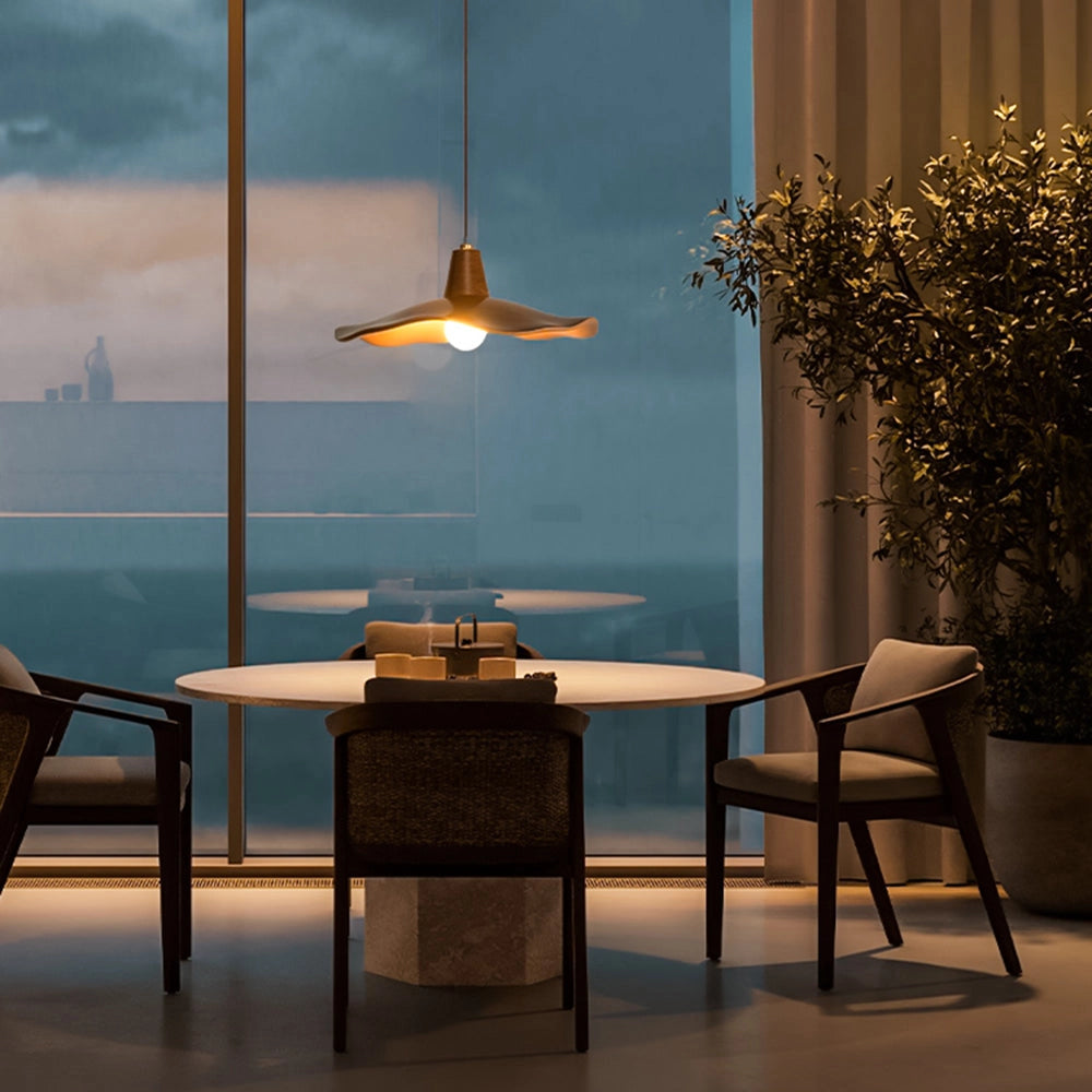 Modern sculptural wood pendant light with a handcrafted organic design, featuring a warm orange hue and a single light source, hanging elegantly in an interior space with a window view.