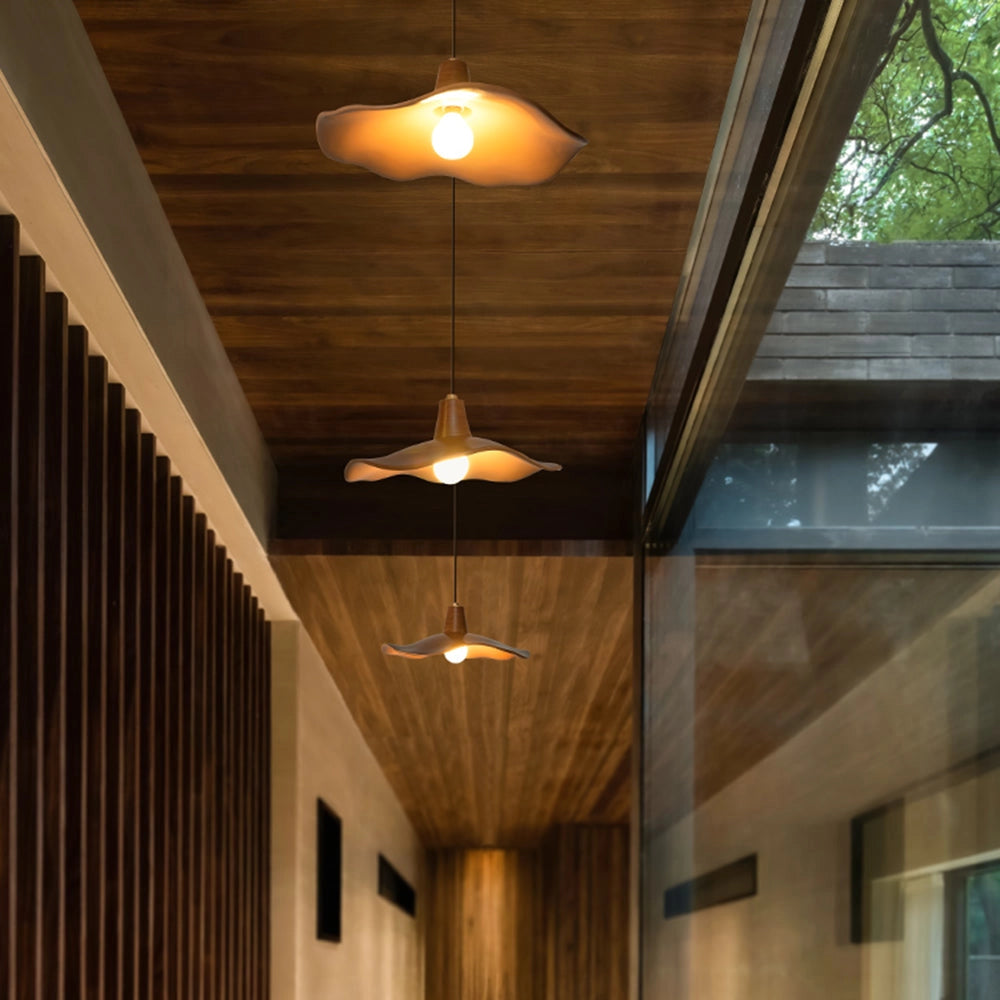 Modern sculptural wood pendant light with a handcrafted organic design, featuring a wooden shade with visible wood grain and stain, elegantly illuminating an interior space with its warm beams of light.
