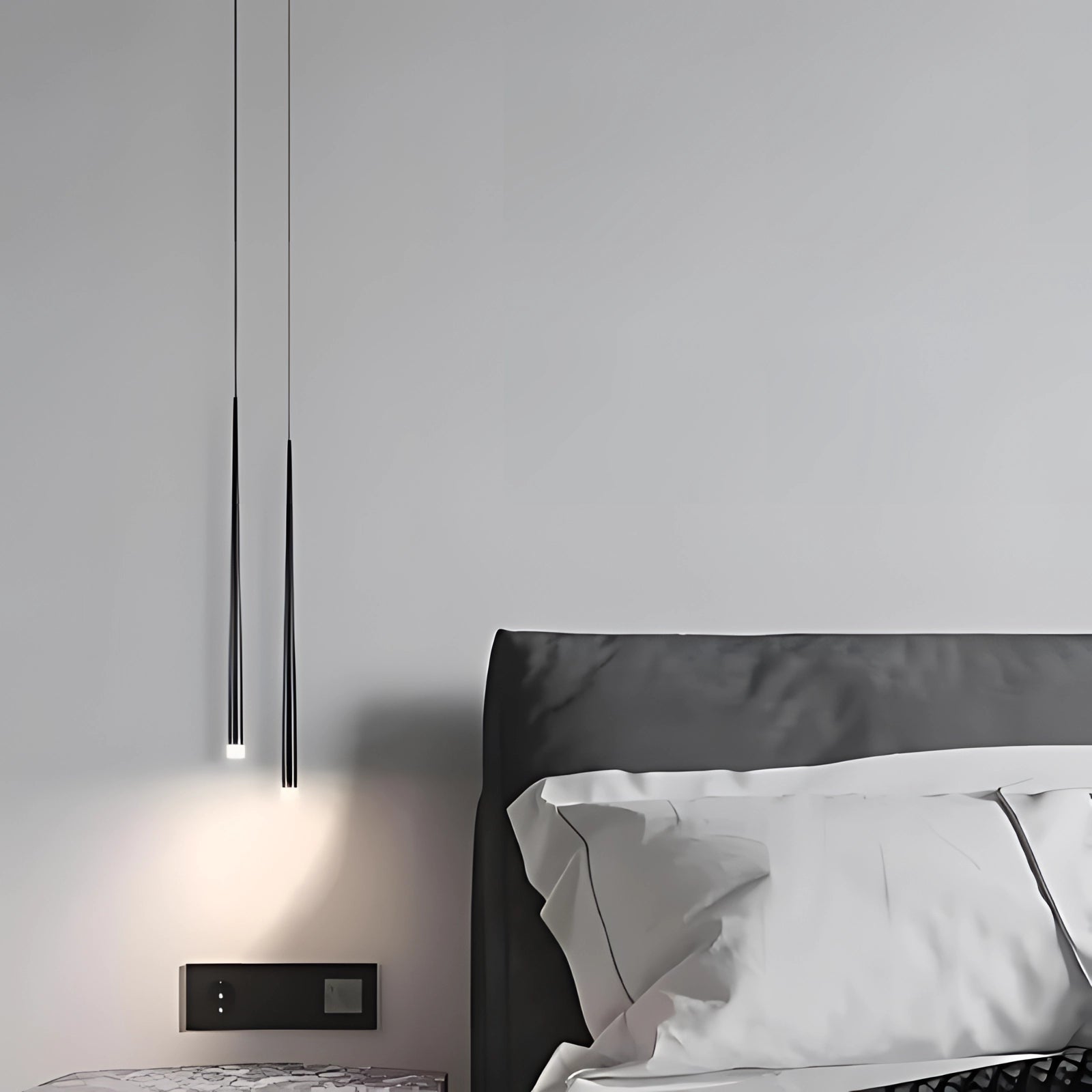 Modern sleek black pendant lights hanging from a high ceiling, providing stylish and contemporary lighting to a room with grey and wood furnishings, including a bed with a grey pillow, and minimalist decor.