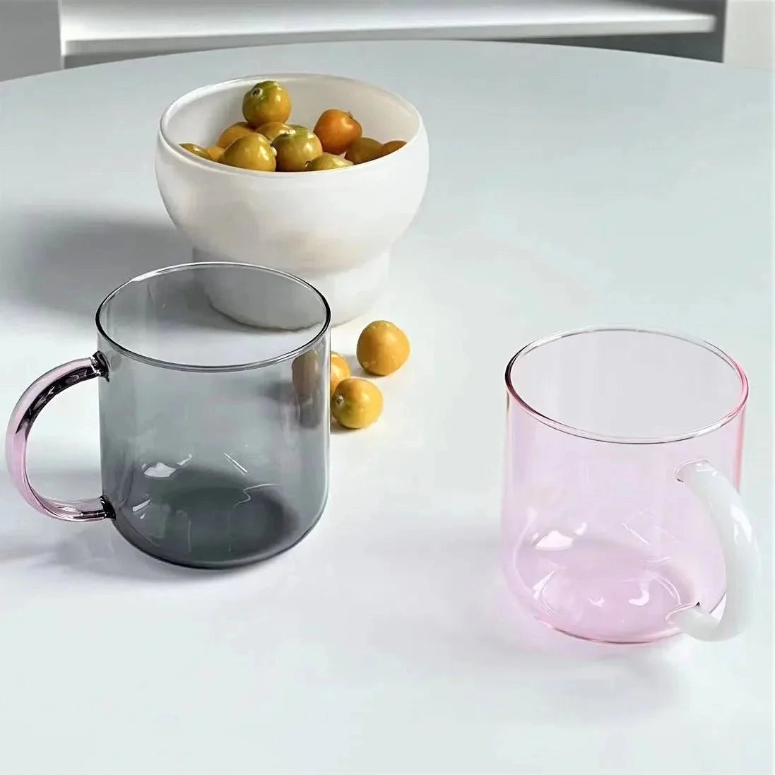 Modern smoke glass mug filled with a citrus-infused beverage, showcasing a stylish grey borosilicate design, set on a table with other dishware.