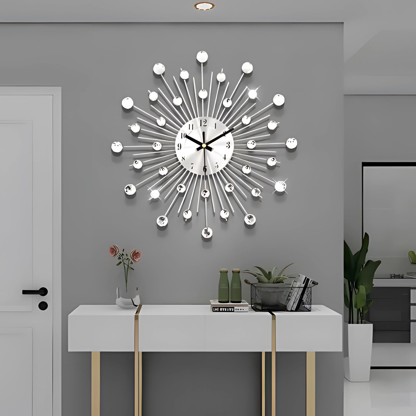 A modern starburst silver wall clock with a unique mid-century design, featuring a round face with silver rays extending outward, set against a grey wall in an interior setting with wooden furniture and green plants.