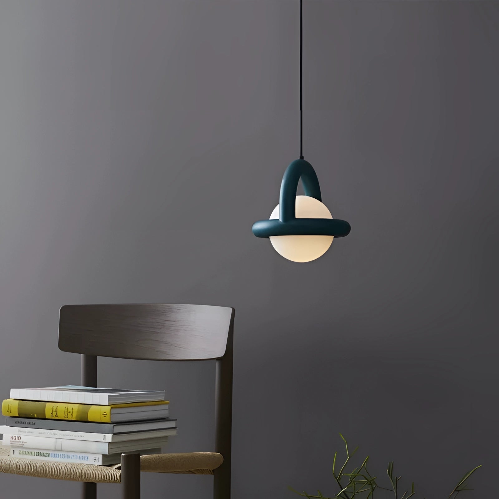 Modern teal orb pendant light with a Scandinavian mid-century style hanging above a wooden table, accompanied by books and a lamp, casting a warm and inviting glow.