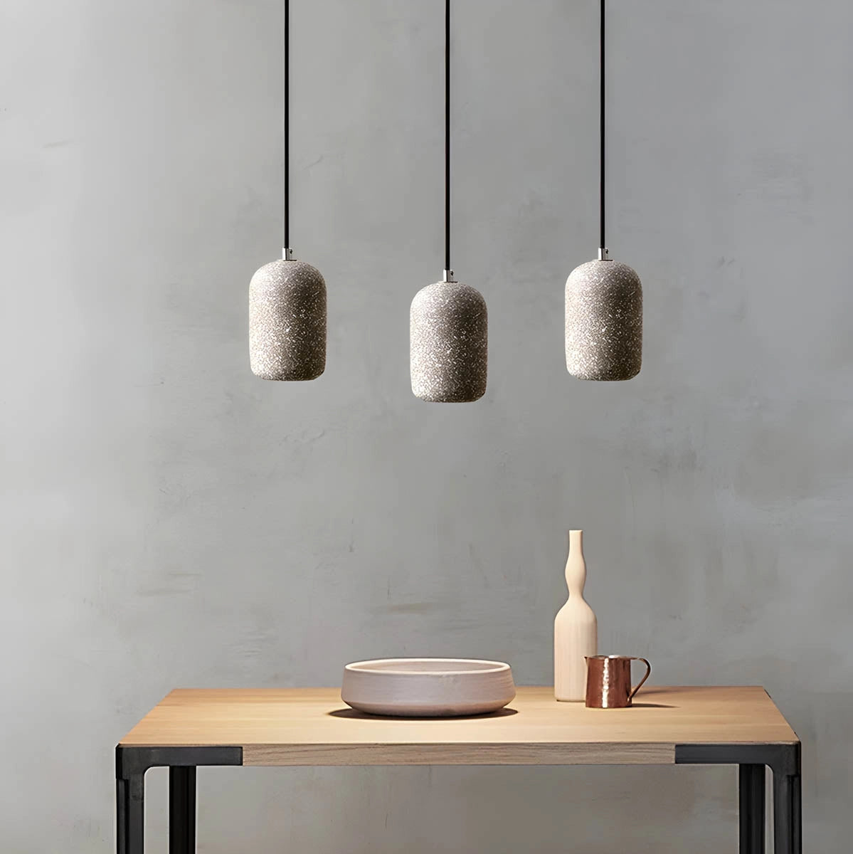 Modern textured concrete pendant lights hanging above a sleek kitchen table with wooden elements and white surfaces, enhancing the contemporary interior design.