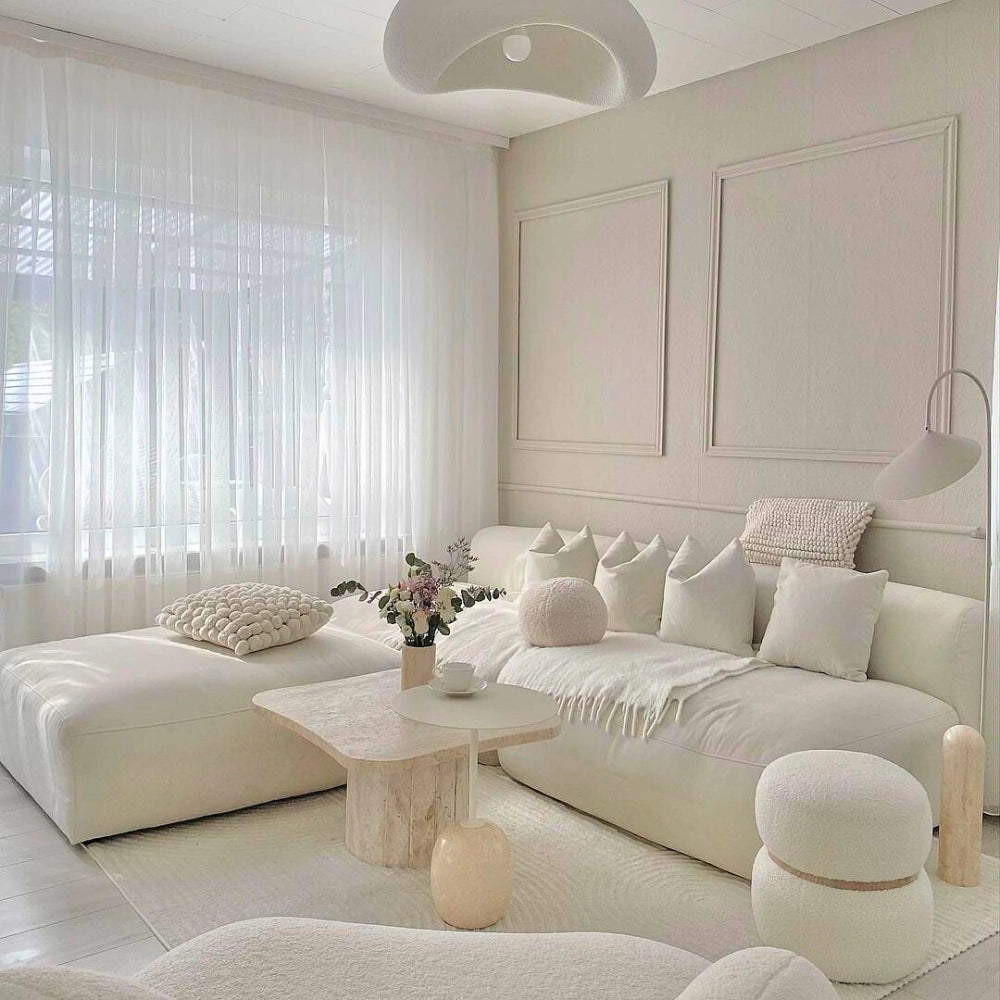 Modern textured pendant light with a minimalist pebble design and stone finish, suspended in a cozy interior setting featuring a couch, pillows, and a table.