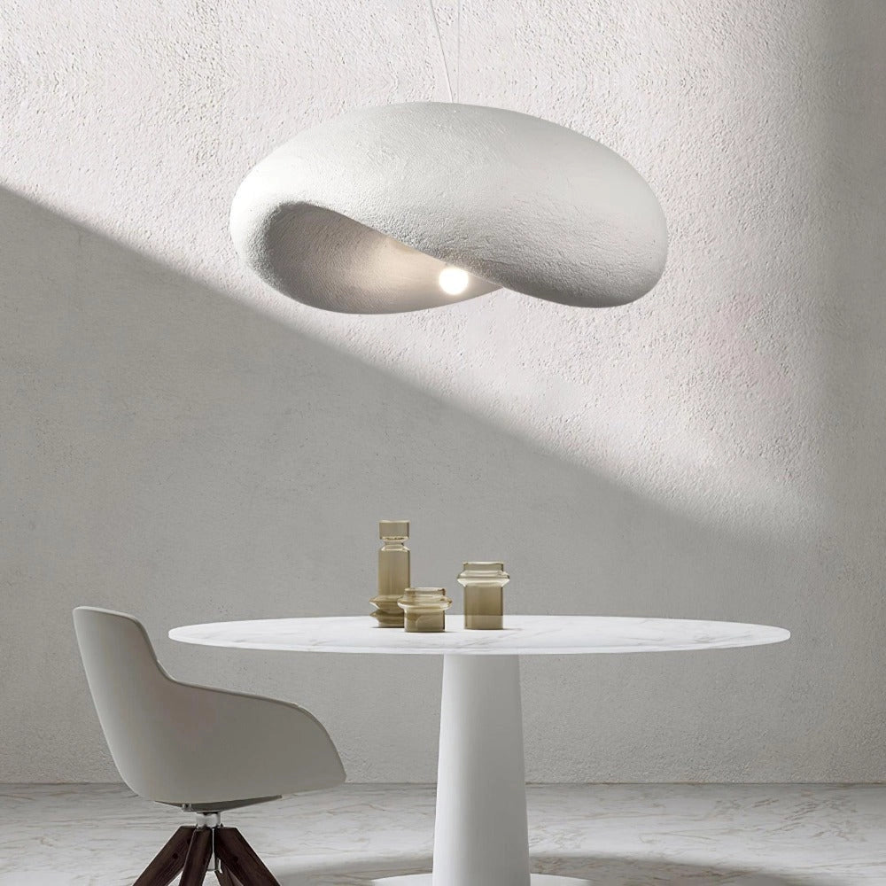 Modern textured pendant light with a minimalist pebble design and stone finish, hanging elegantly over a wooden table in a stylish interior setting.
