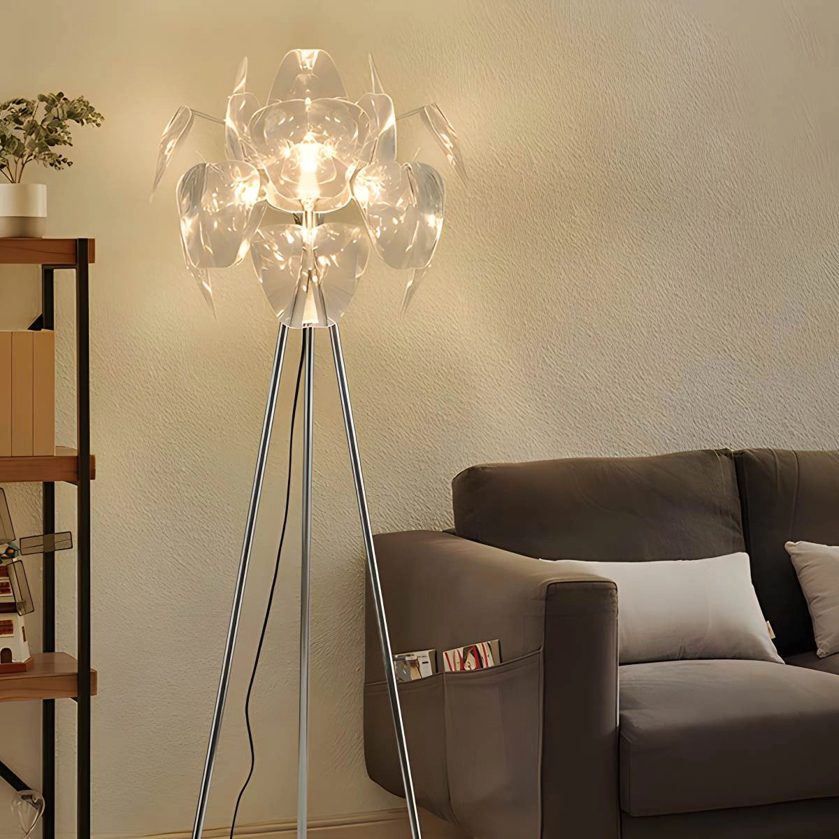 Modern tri-leg floor lamp with a petal design and a clear acrylic globe, placed in a stylish interior with furniture including a grey couch, wooden table, and art decor.