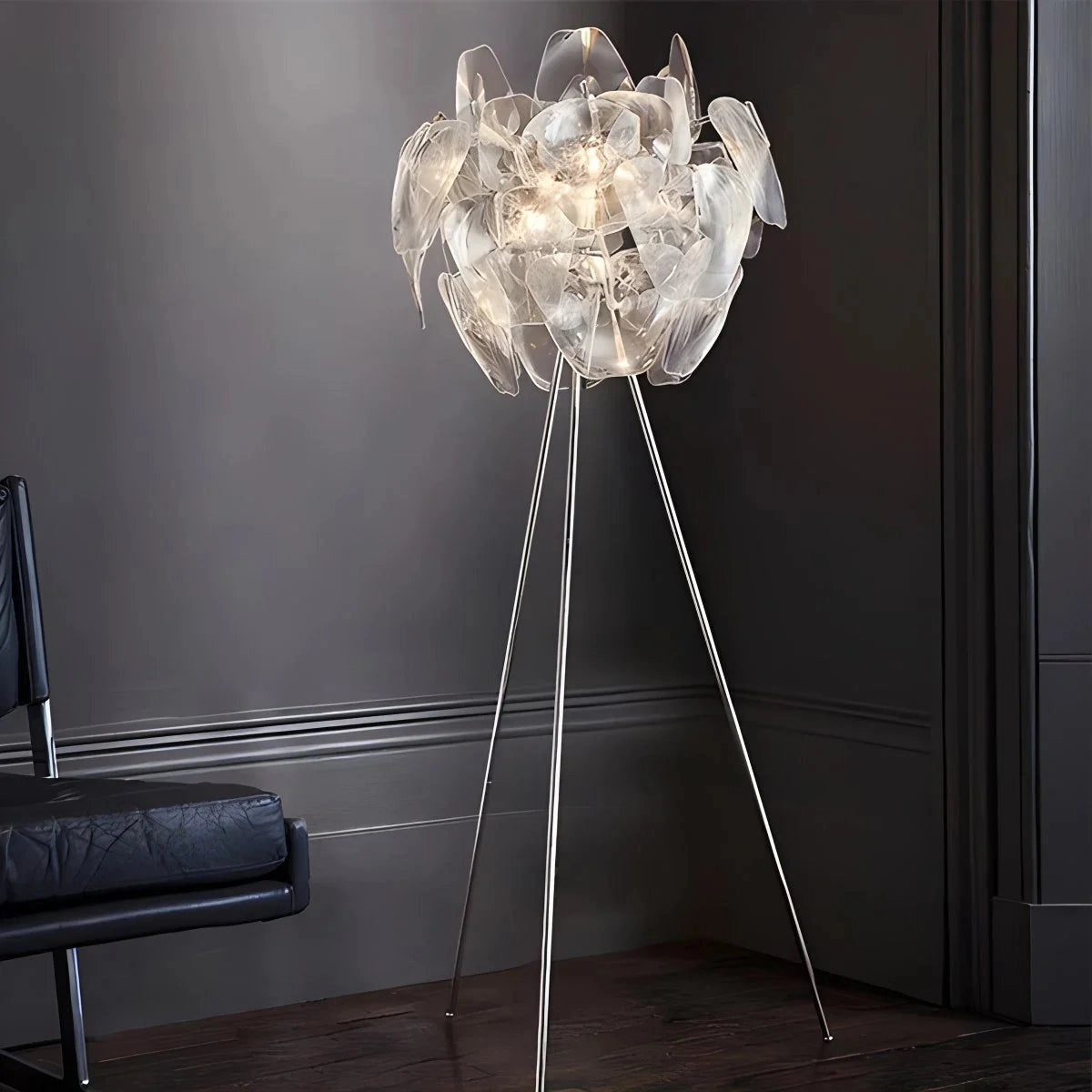 Modern tri-leg floor lamp with petal design, featuring a clear acrylic globe, likely displayed in a contemporary setting with grey accents and wooden elements.