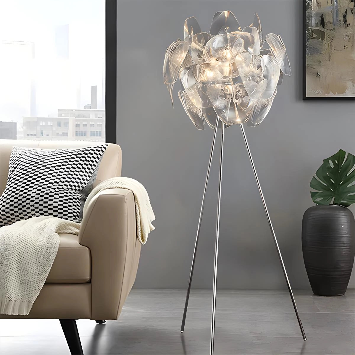 Modern tri-leg floor lamp with petal design and clear acrylic globe, placed in a stylish living room with grey couch and flowerpot.