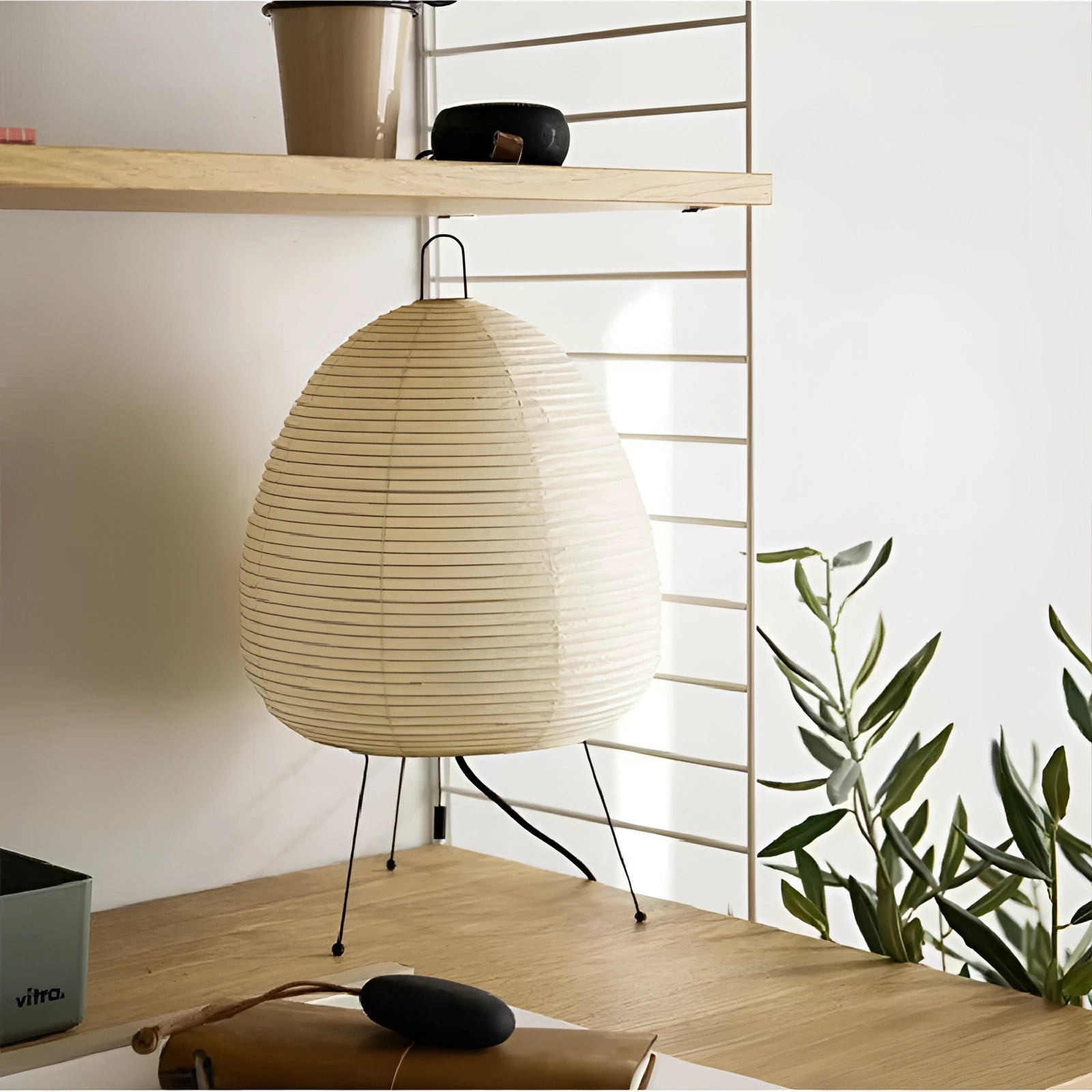Modern tripod floor lamp with a Japanese-inspired design, featuring a wooden base and rectangular grey lampshade, illuminating a softly lit interior space with ambient light.