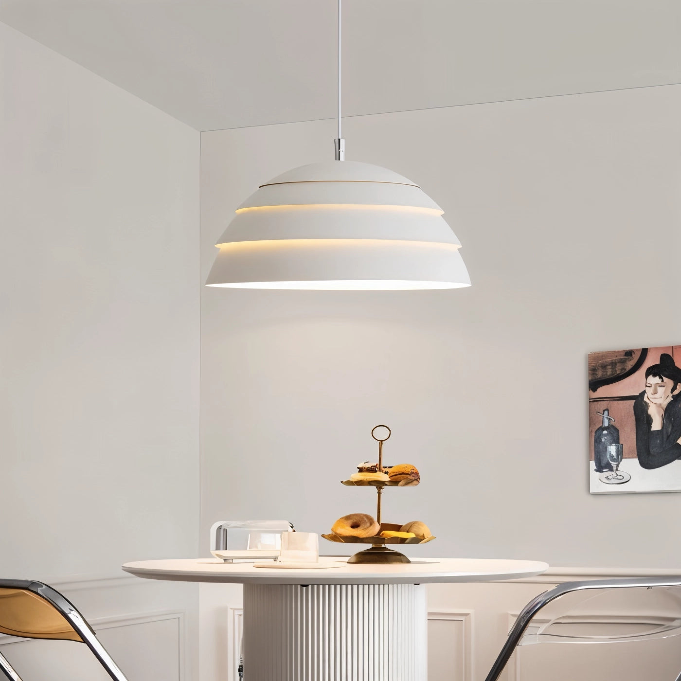Modern white layered pendant light fixture hanging from the ceiling in a minimalist indoor setting, surrounded by wooden cabinetry and shelving, with a sleek table underneath.