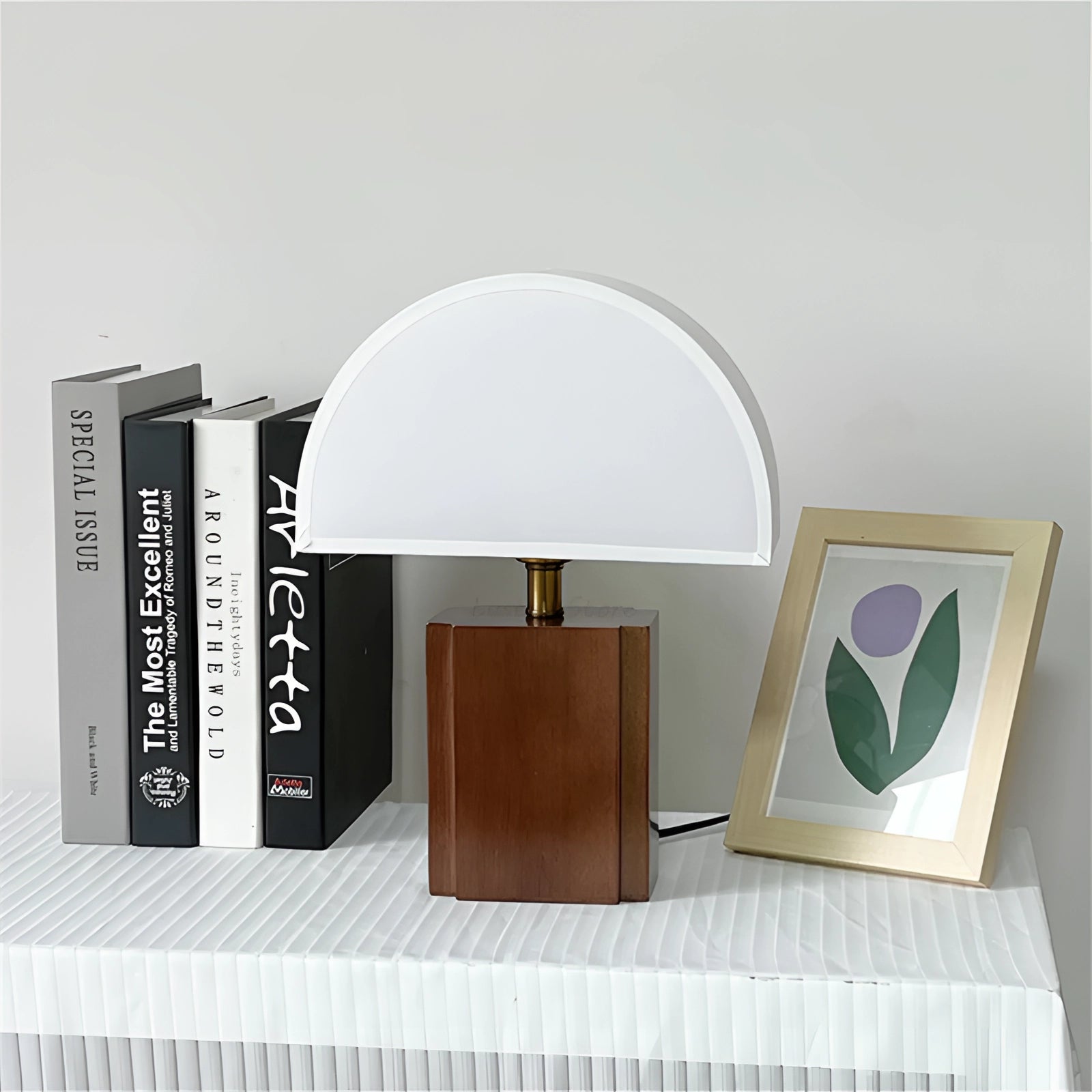 Modern wooden half-dome lamp with a minimalist design, featuring a rectangular wooden base placed on a table, surrounded by decor elements like shelving and a plant.