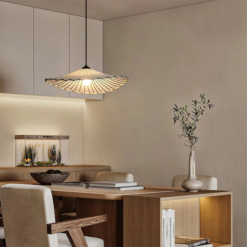 Modern wooden pendant lamp with a sculptural design hanging in a stylish interior setting, featuring wooden and grey elements, with nearby furniture and a plant enhancing the contemporary decor.