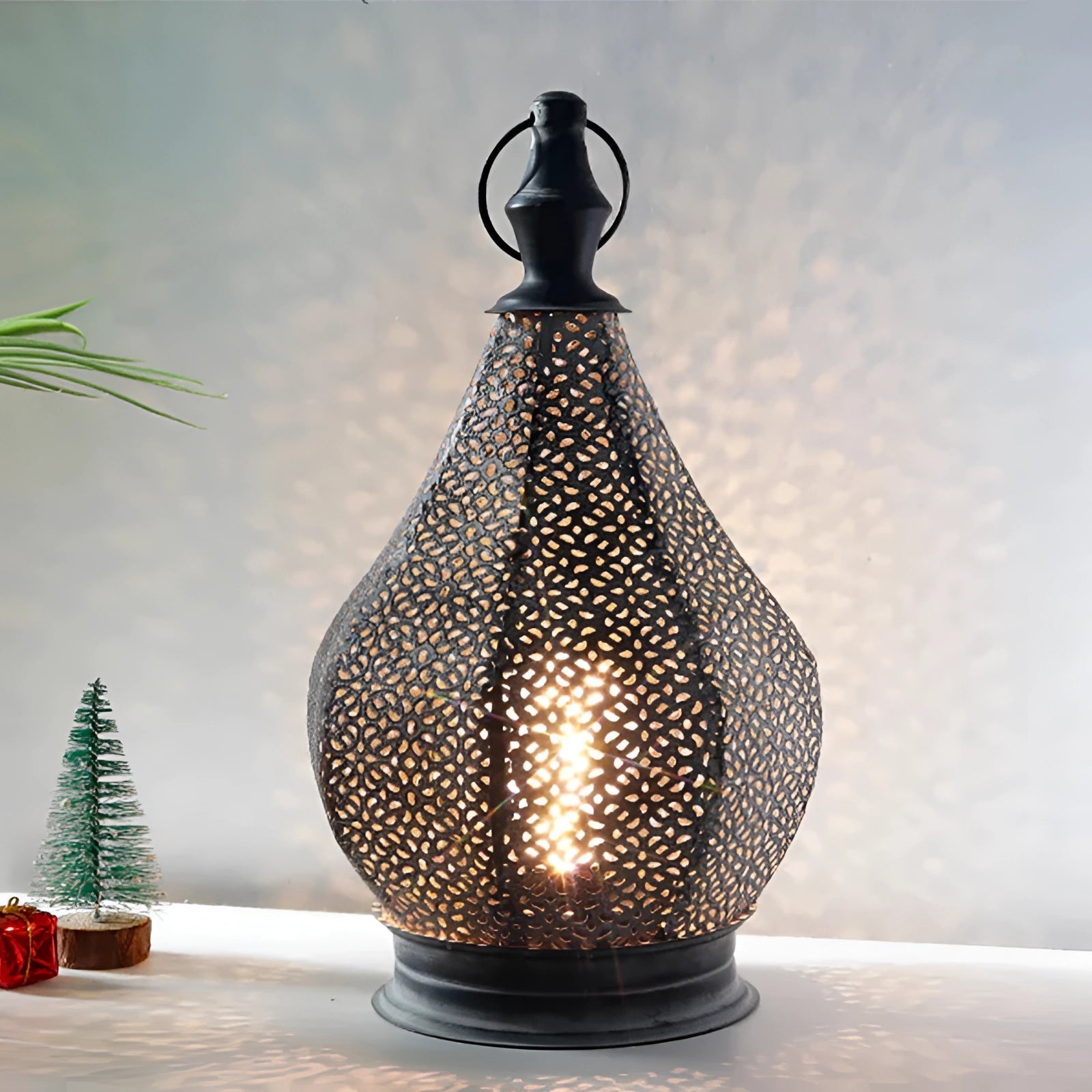 Handmade Moroccan metal table lamp with an ethnic design, featuring intricate patterns on the shade, placed on a wooden table alongside a small potted plant.