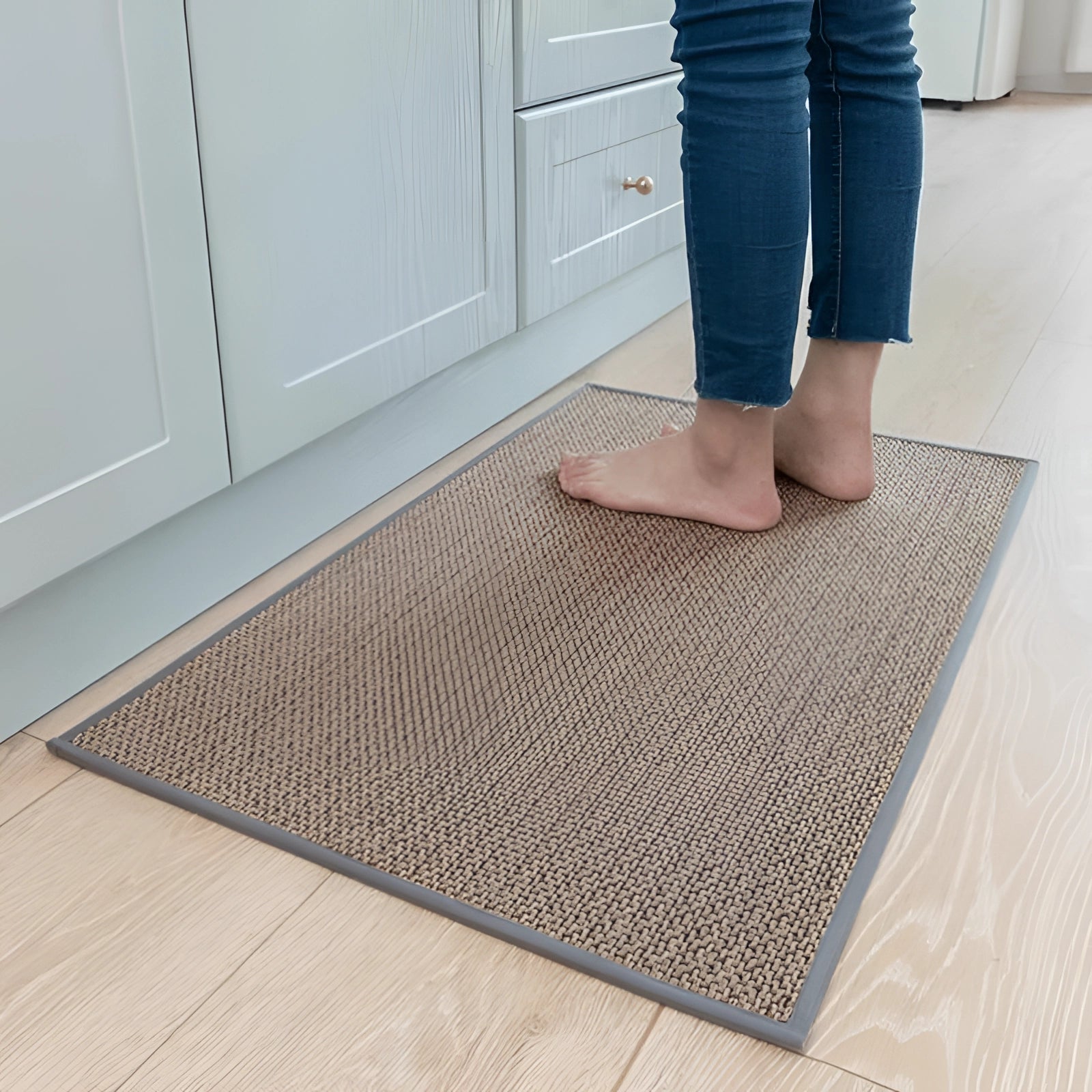 Non-slip beige kitchen mat with a gray beige color, measuring 50 x 80 cm, placed on a wooden floor. The durable washable sisal rug is rectangular in shape and complements cabinetry in the surrounding area.