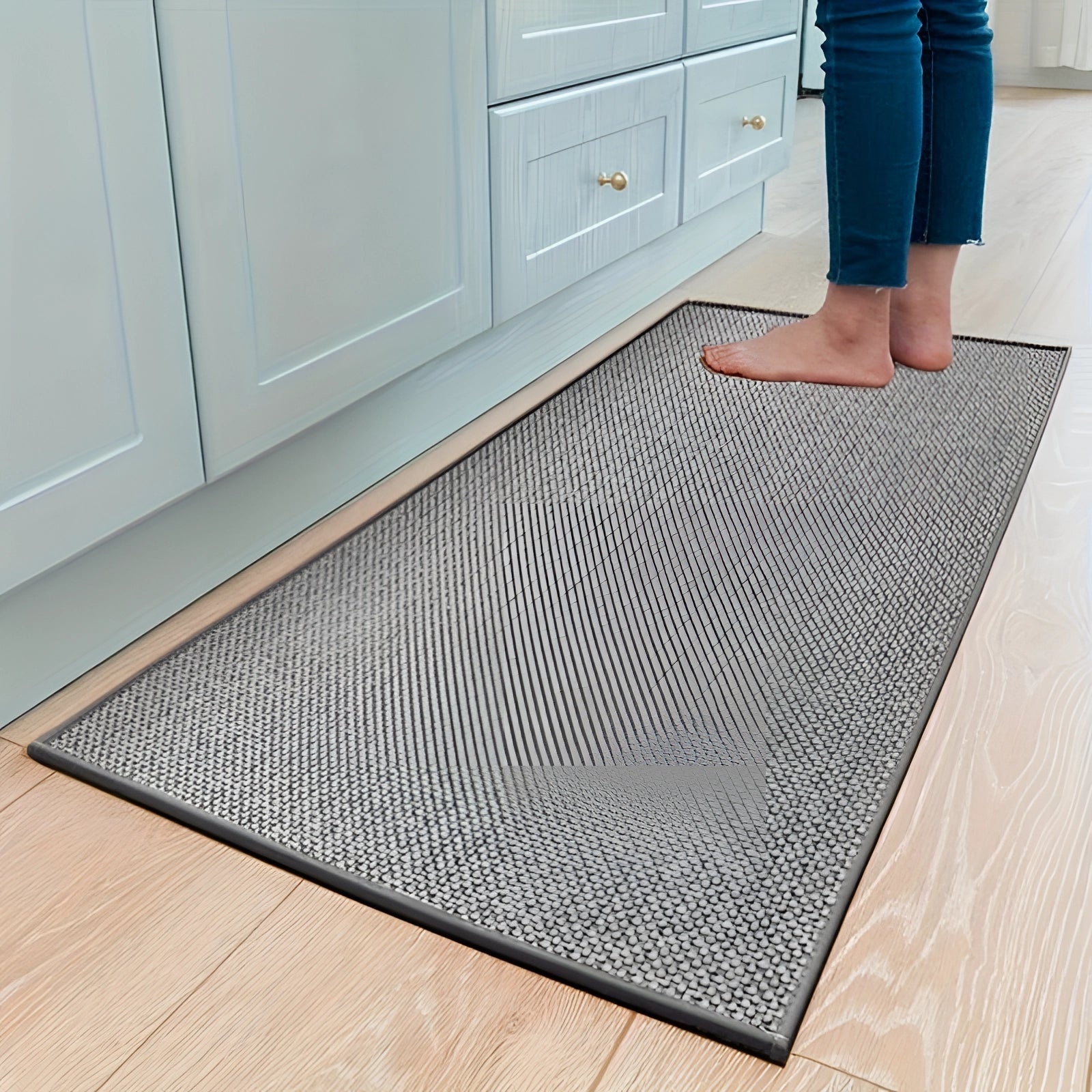 
A gray rectangular non-slip kitchen mat made from durable sisal material, placed on a wooden floor in front of kitchen cabinetry.